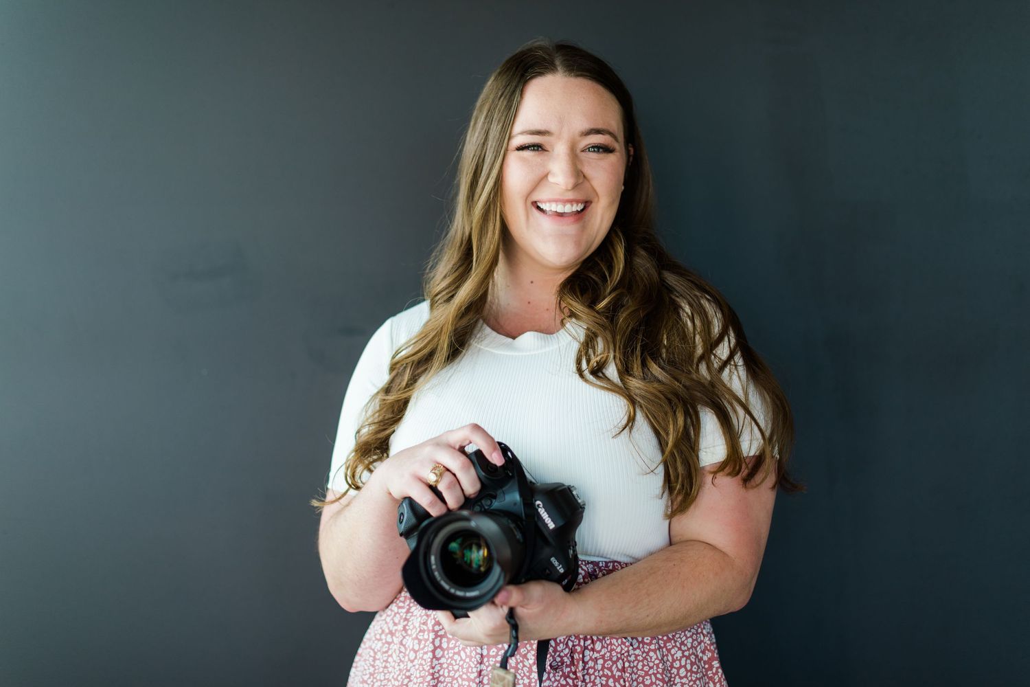 A professional photographer smiles while holding camera against dark background.