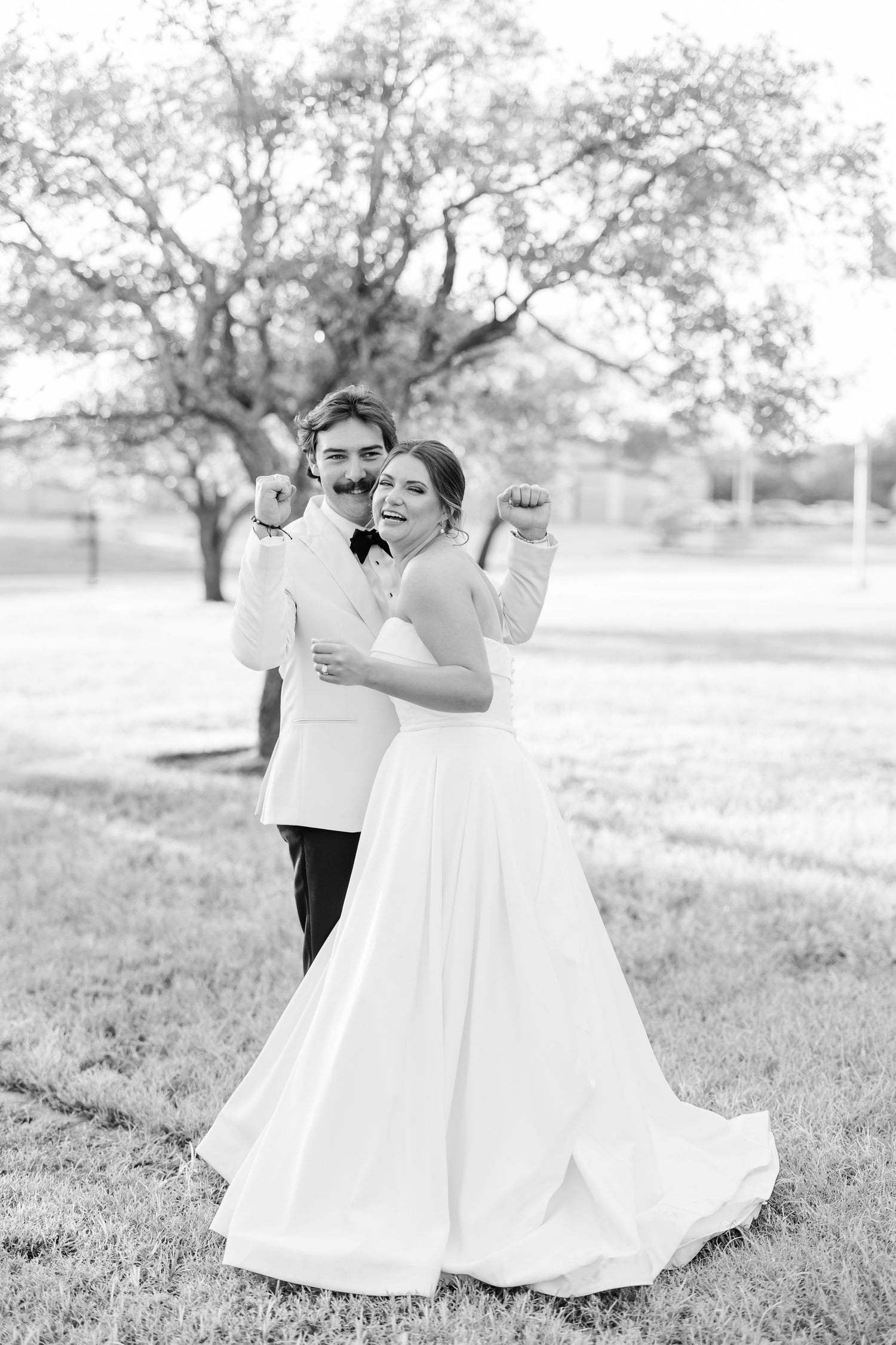 Black and white photo of celebratory moment on a grassy lawn with trees in background.