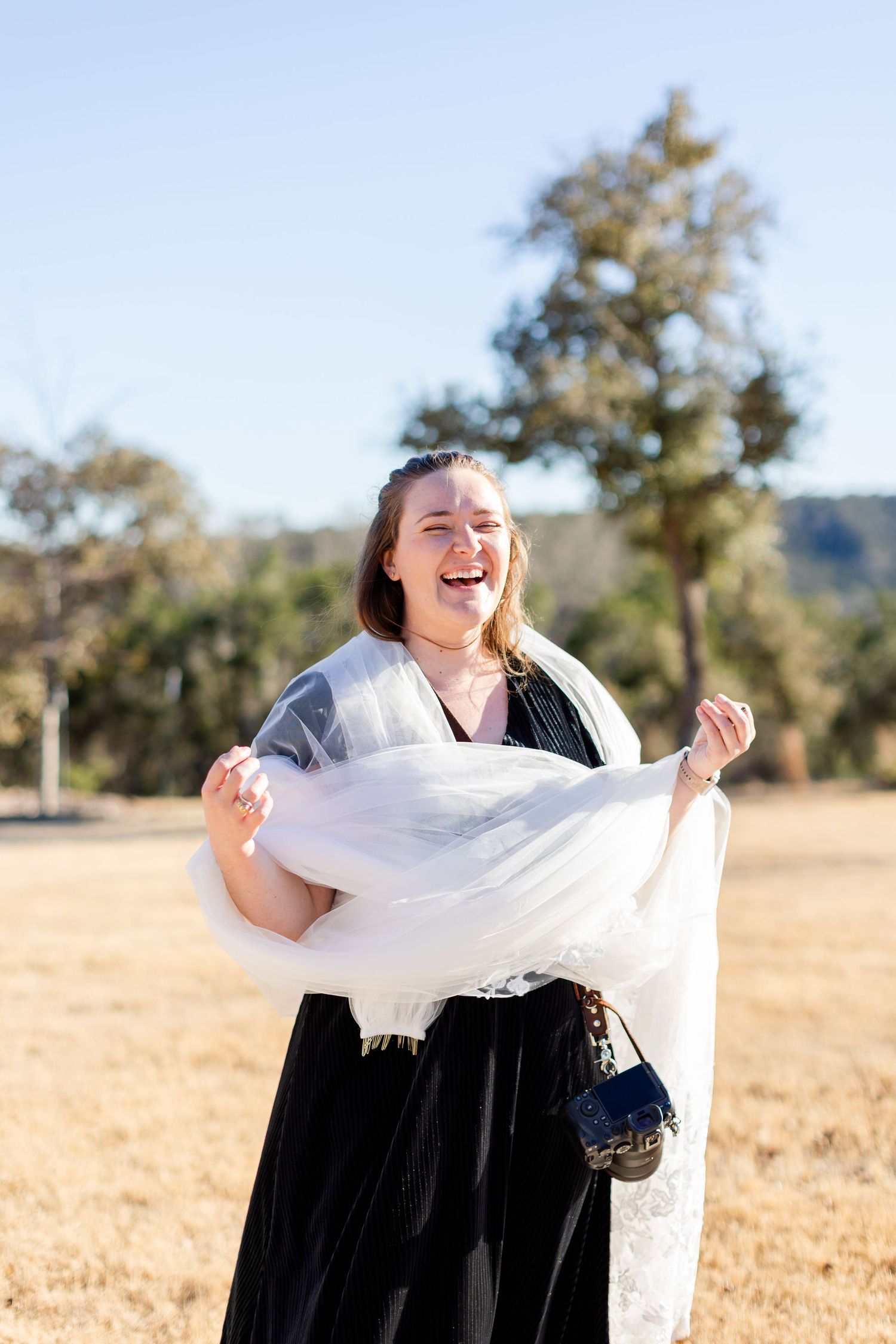 A woman in a black dress and white shawl dances joyfully in a golden field at sunset.