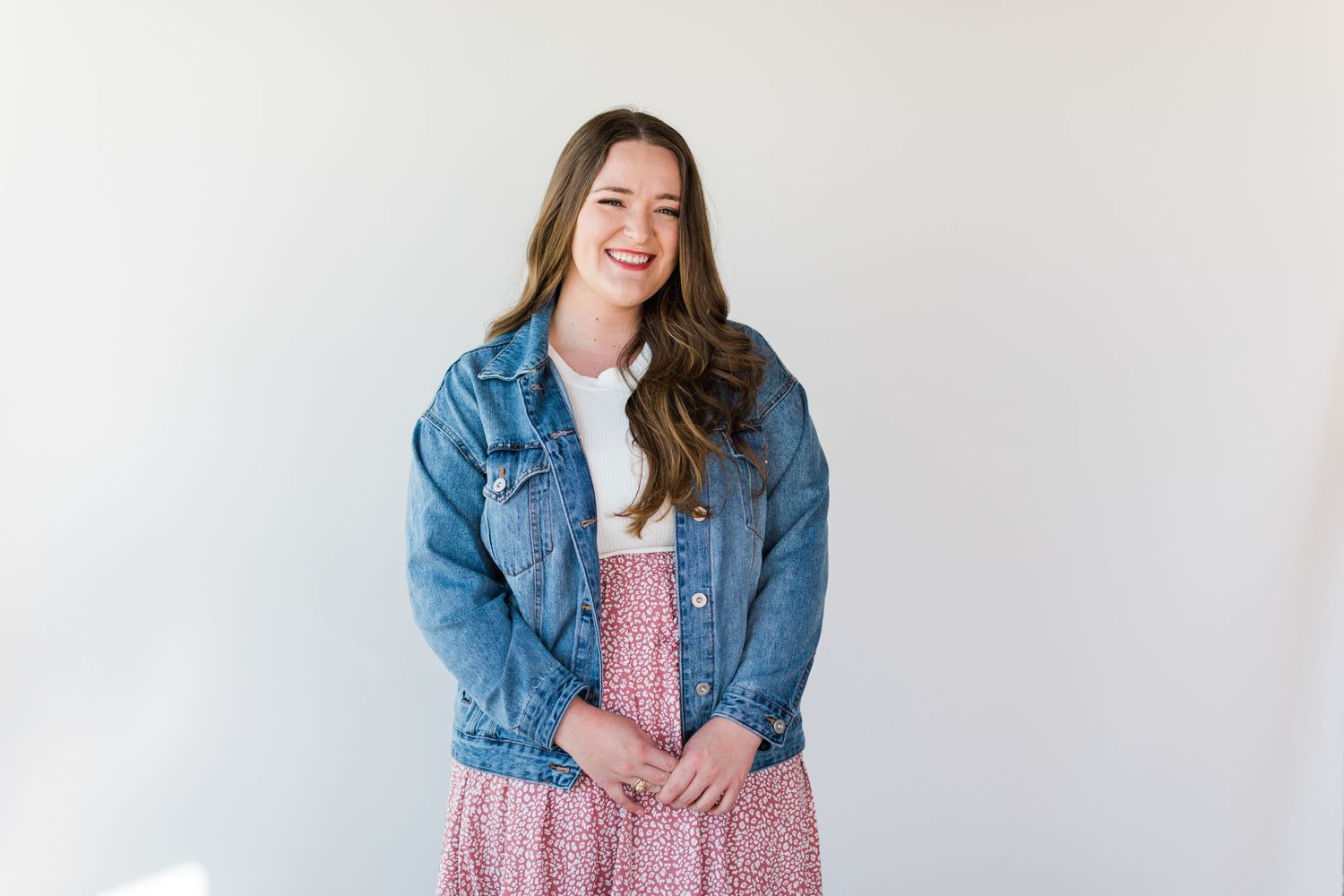 A casual portrait against white backdrop wearing denim jacket and pink skirt.