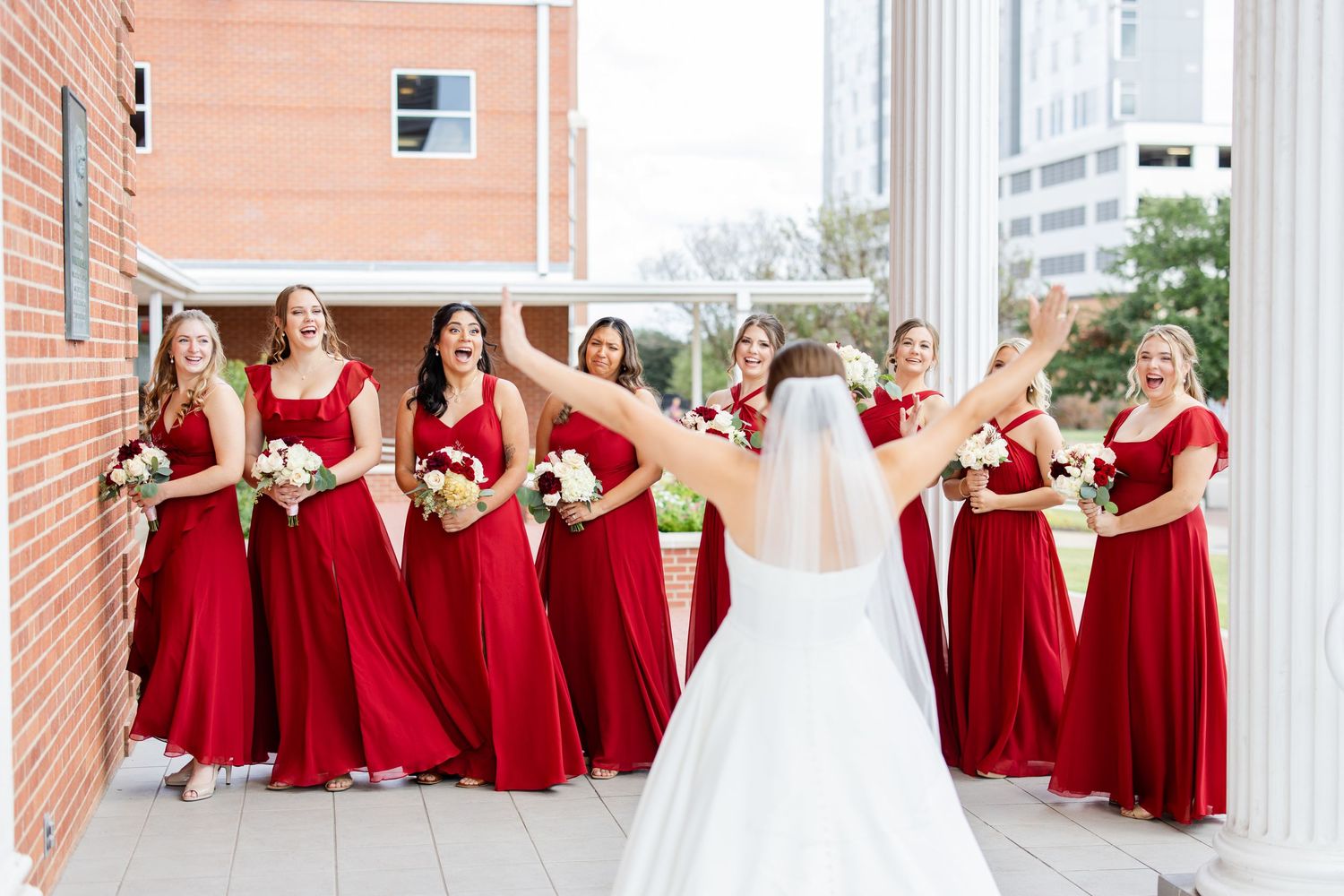 Bridesmaids in red dresses pose with the bride in a courtyard.