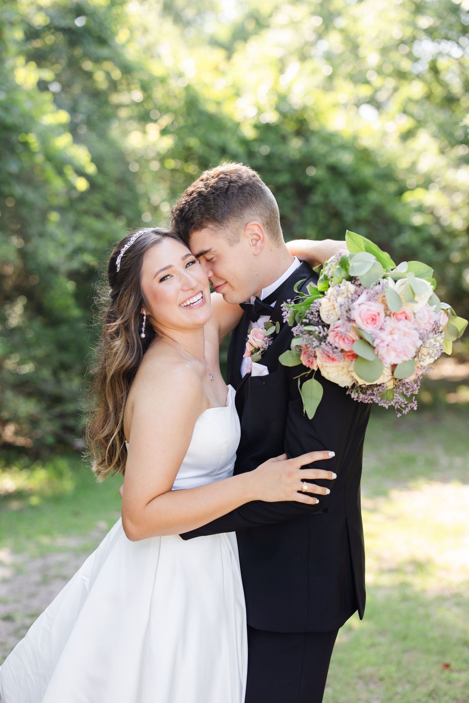 A couple shares a romantic moment with pink flowers in an outdoor garden setting.
