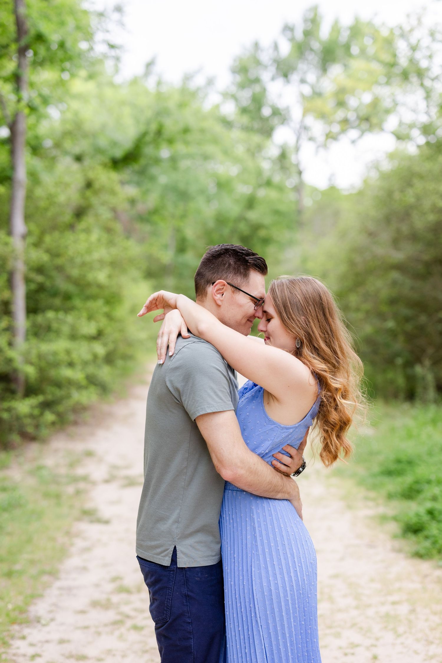 Romantic couple embracing on a nature trail surrounded by lush green trees.