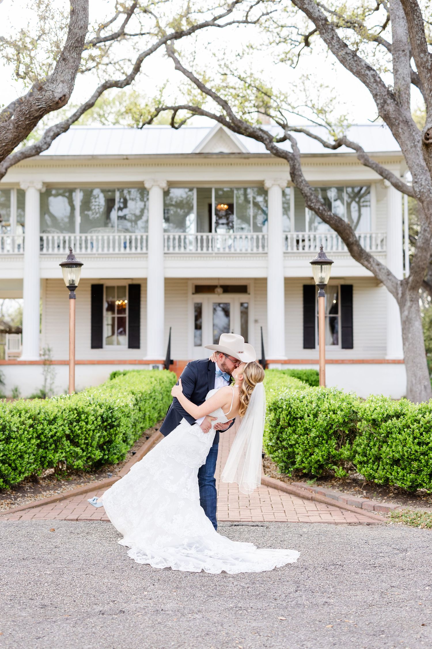 Classic wedding pose in front of white southern mansion with flowing veil.