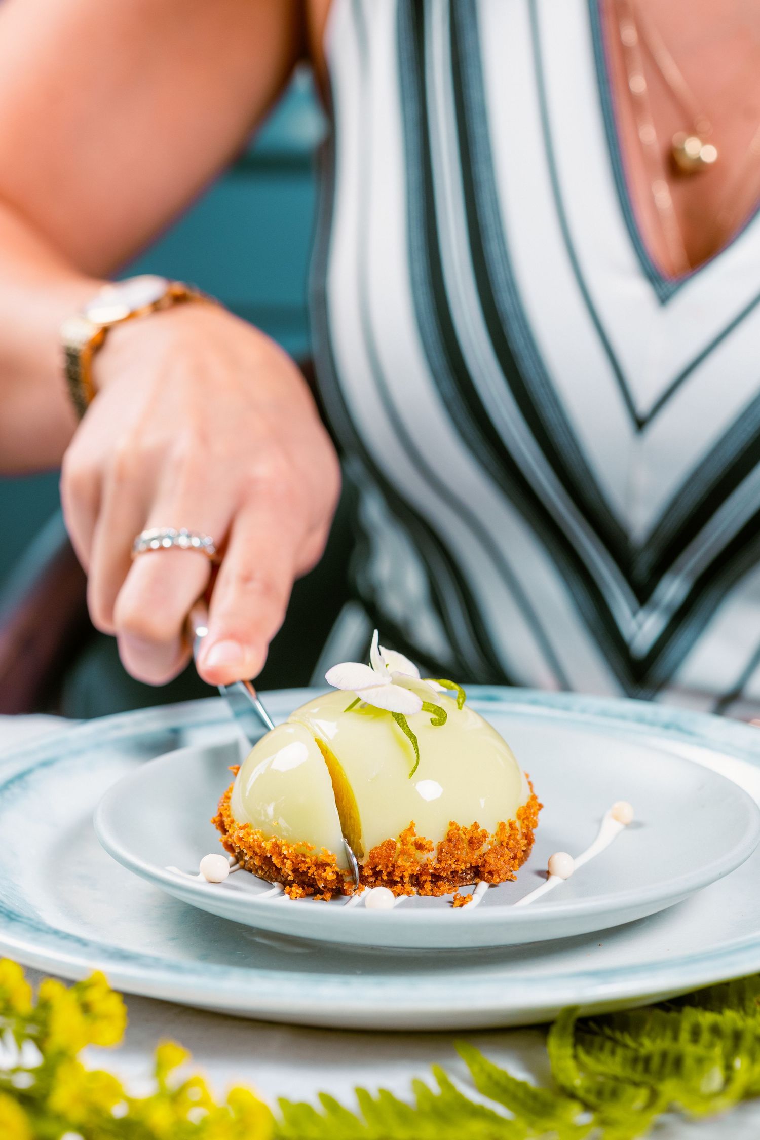 Hands plating a delicate lemon dessert with crumb crust on white dishes.