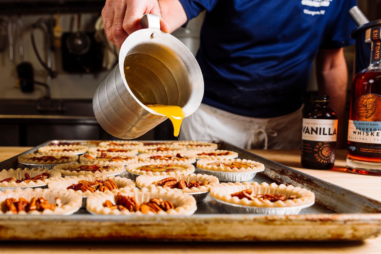 Close-up of hands preparing food on a metal baking sheet with ingredients and sauces.