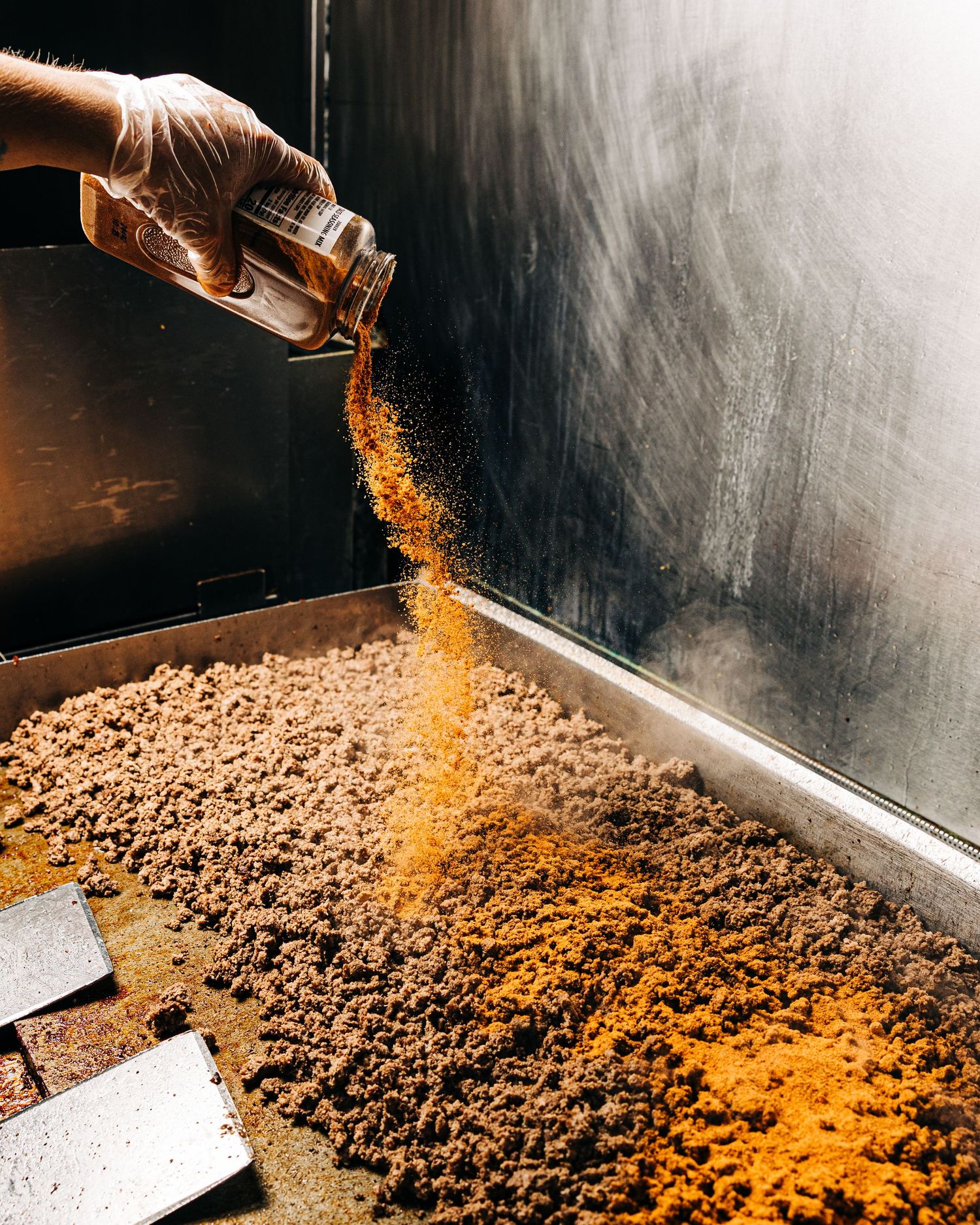Spices being ground and sprinkled onto a dark metal surface in dramatic lighting.