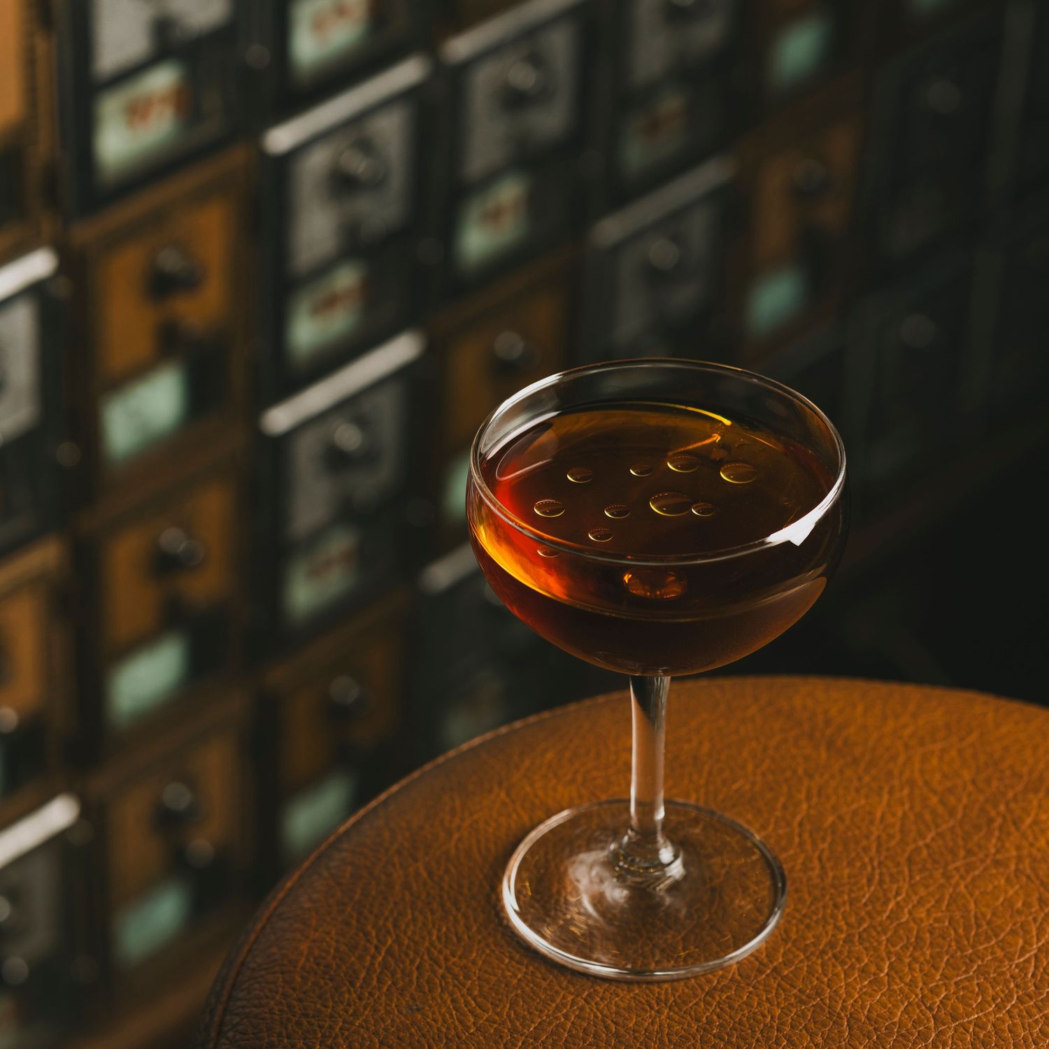 Elegant cocktail glasses with amber-colored drinks on a textured leather surface in moody lighting.