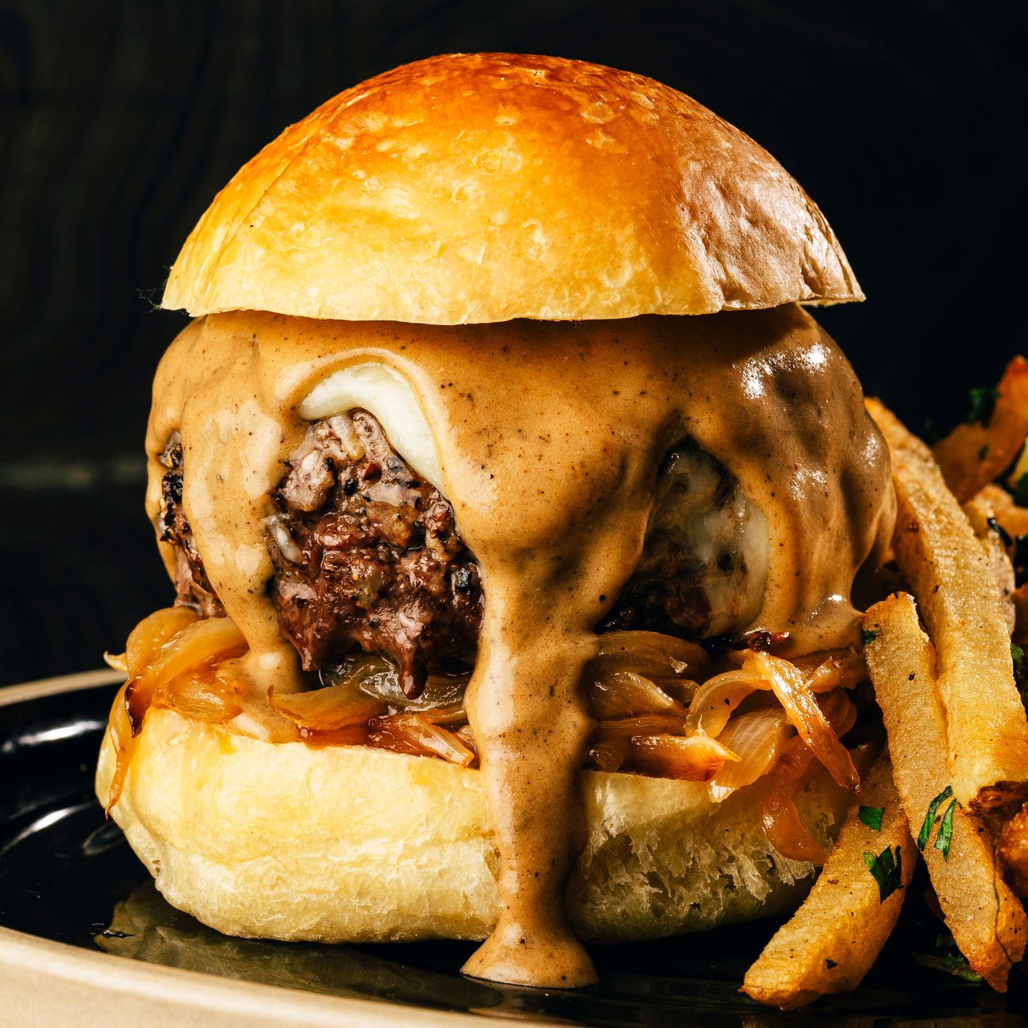 Gourmet cheeseburger with melted cheese and fries on dark background.