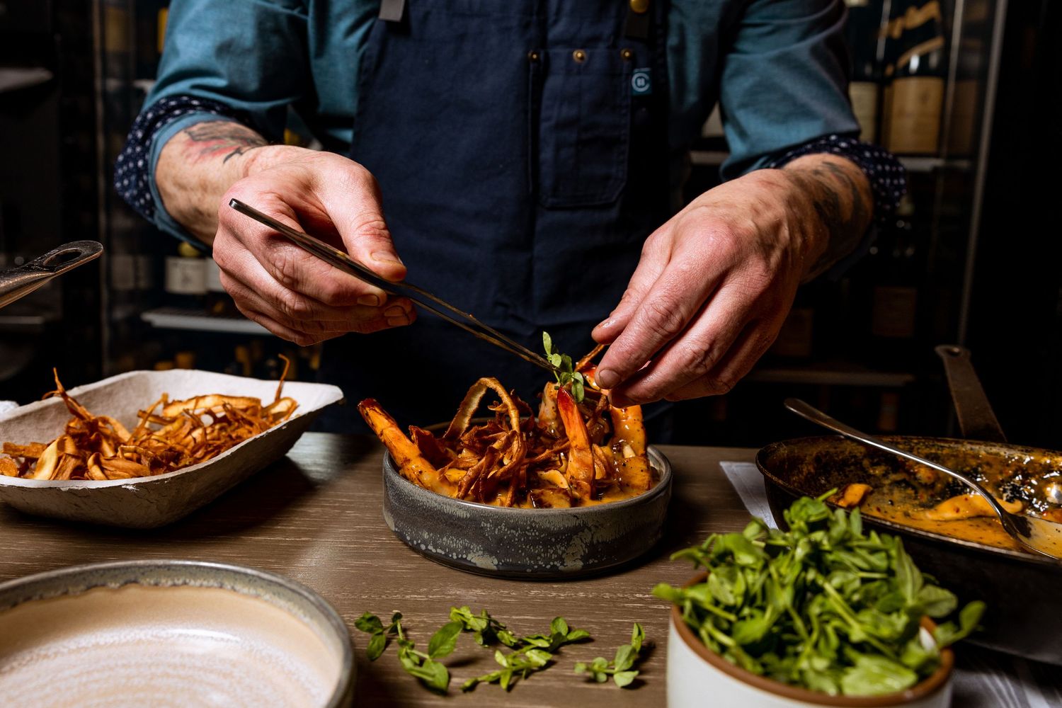 Chef hands preparing and plating gourmet dishes in restaurant kitchen.
