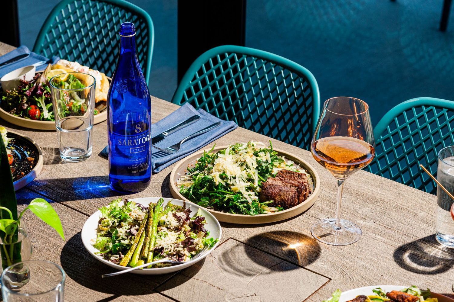 Outdoor restaurant dining setup with turquoise chairs and plated meals.