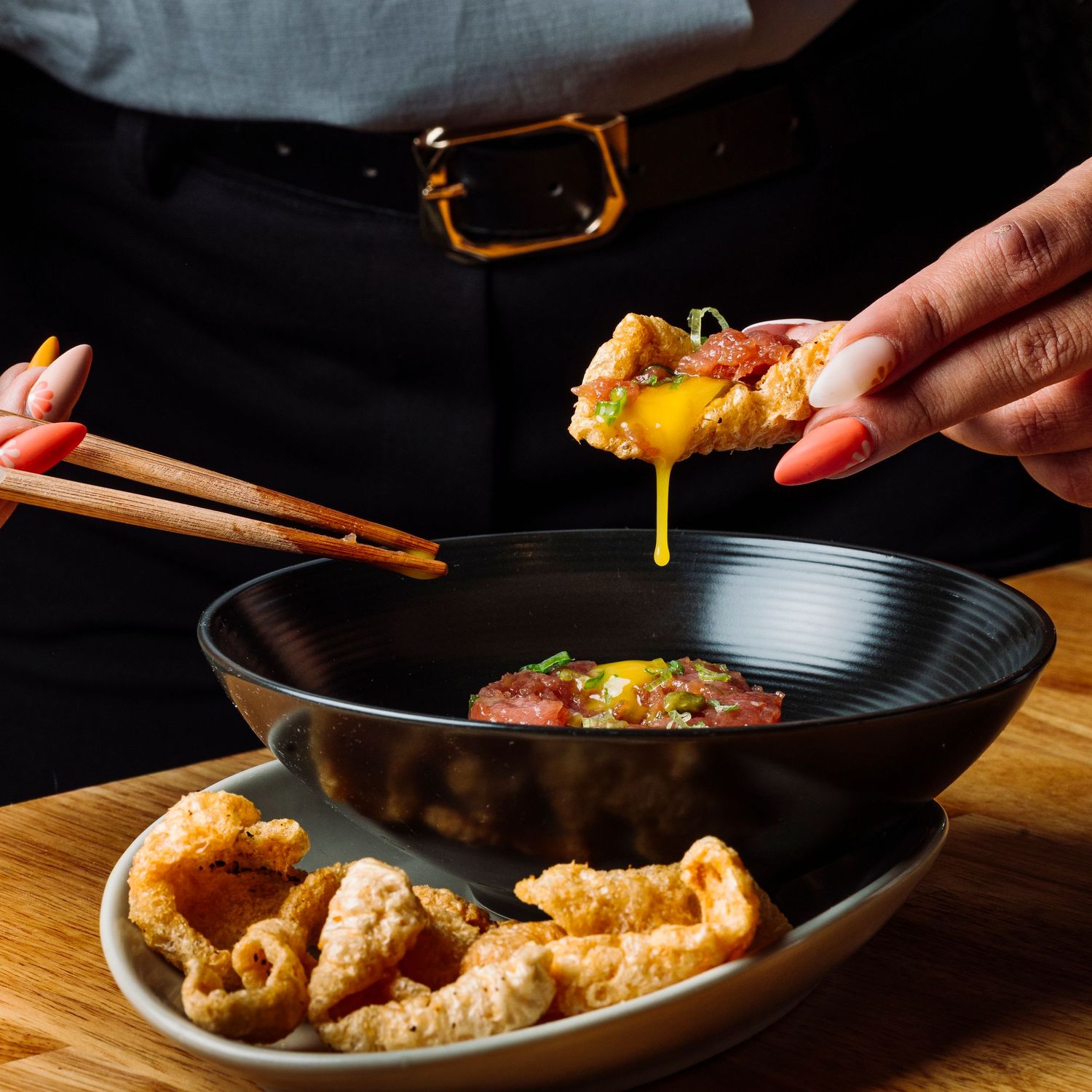 Cooking process showing hands preparing food in a black pan on wooden surface.