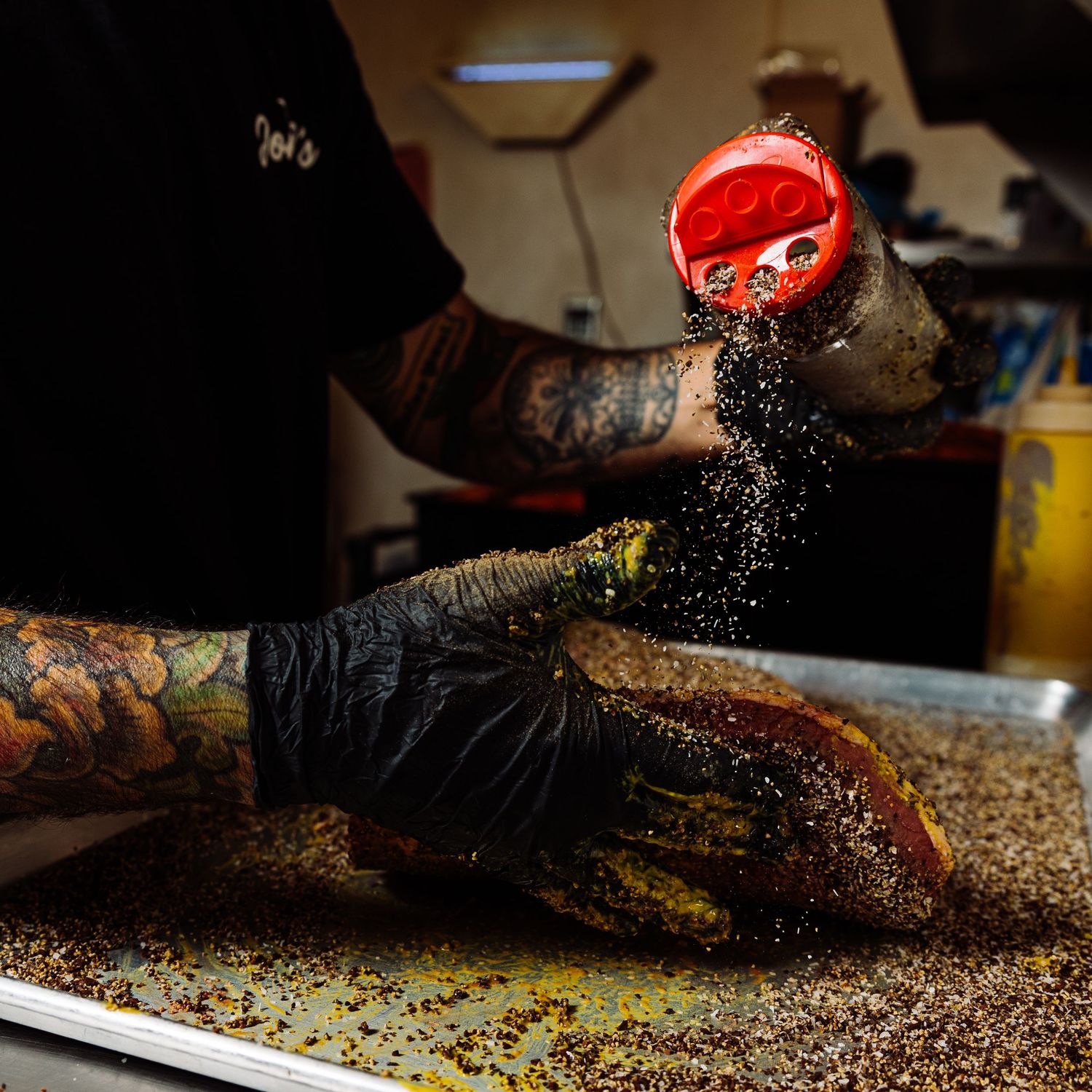 Chef hands in black gloves seasoning and preparing food in a dark professional kitchen.