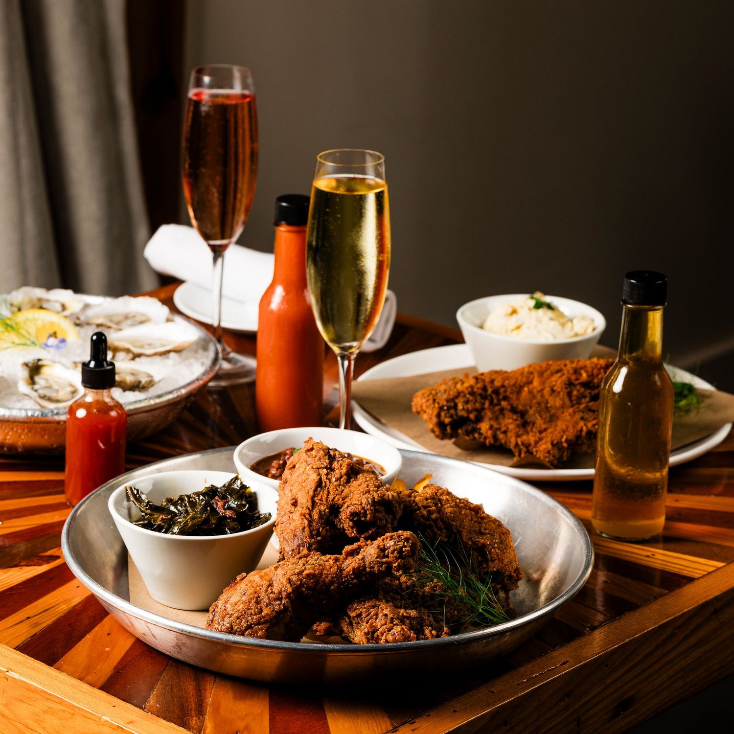 Crispy fried chicken dinner served with sides and drinks on wooden table in warm lighting.