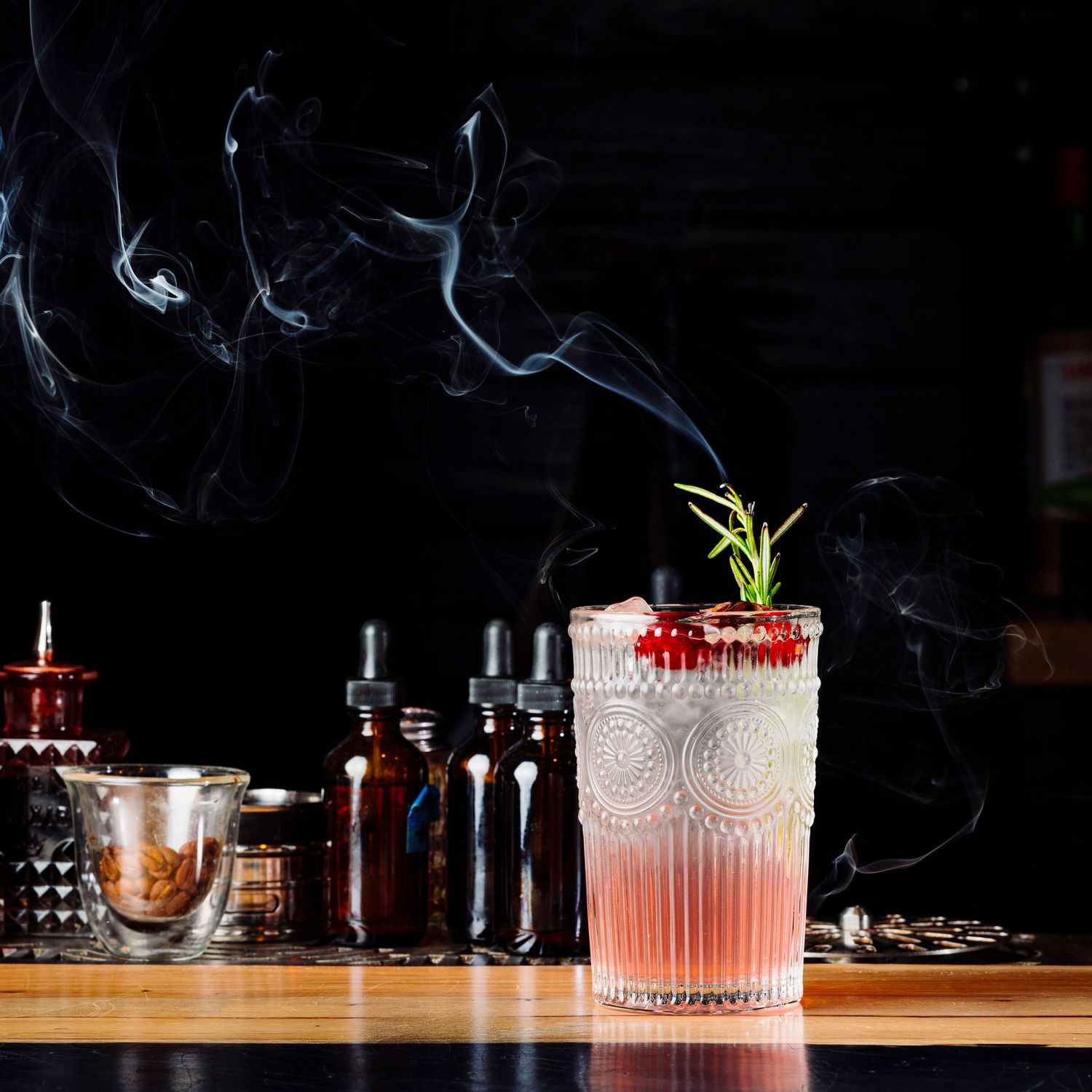 Smoky craft cocktail garnished with rosemary and berries in an ornate glass.