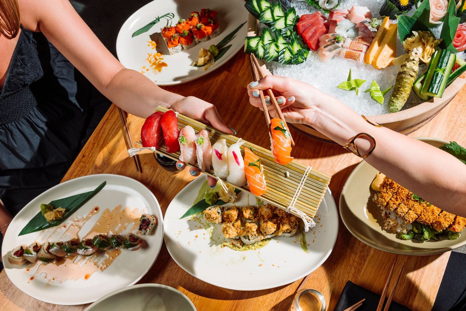 Multiple hands reaching for food across a dining table with various dishes.