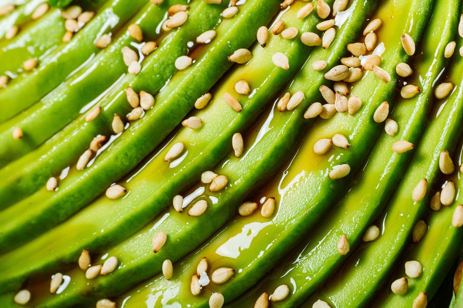 Fresh green sliced avocado garnished with sesame seeds arranged in parallel rows on a wooden surface.