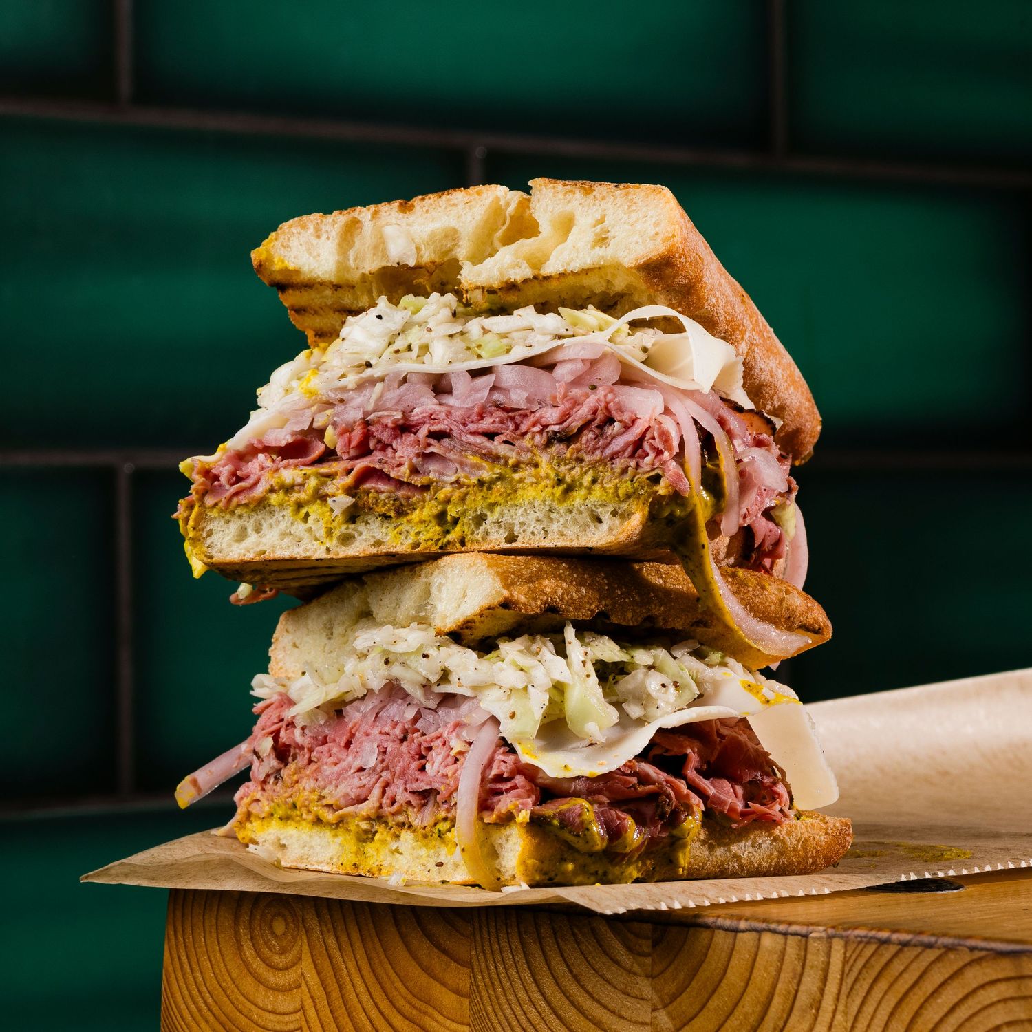 Towering deli sandwich stacked with pastrami, coleslaw and mustard on rye bread.