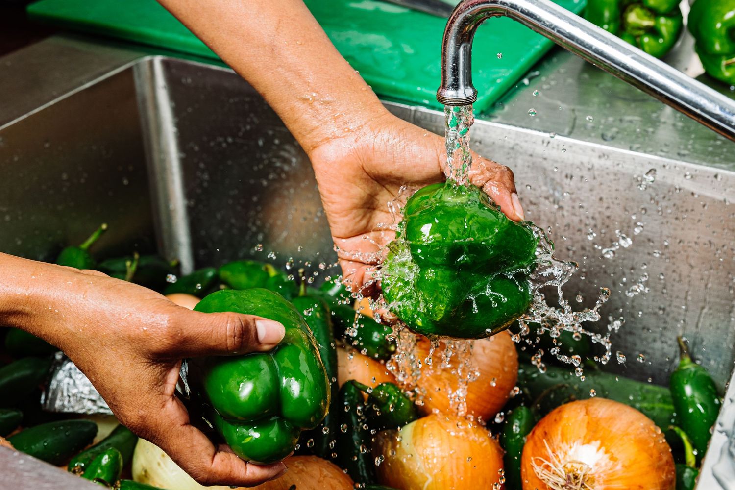 Fresh vegetables being washed and prepared under running water in kitchen sink.