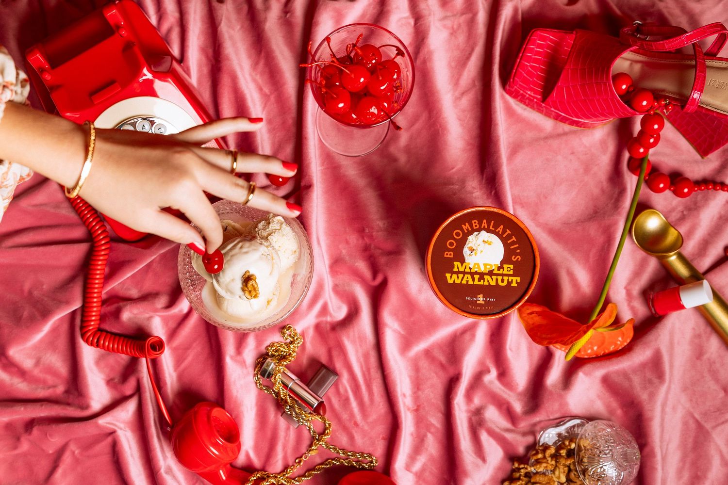 Overhead view of red-themed drinks and decorative items on pink satin fabric.