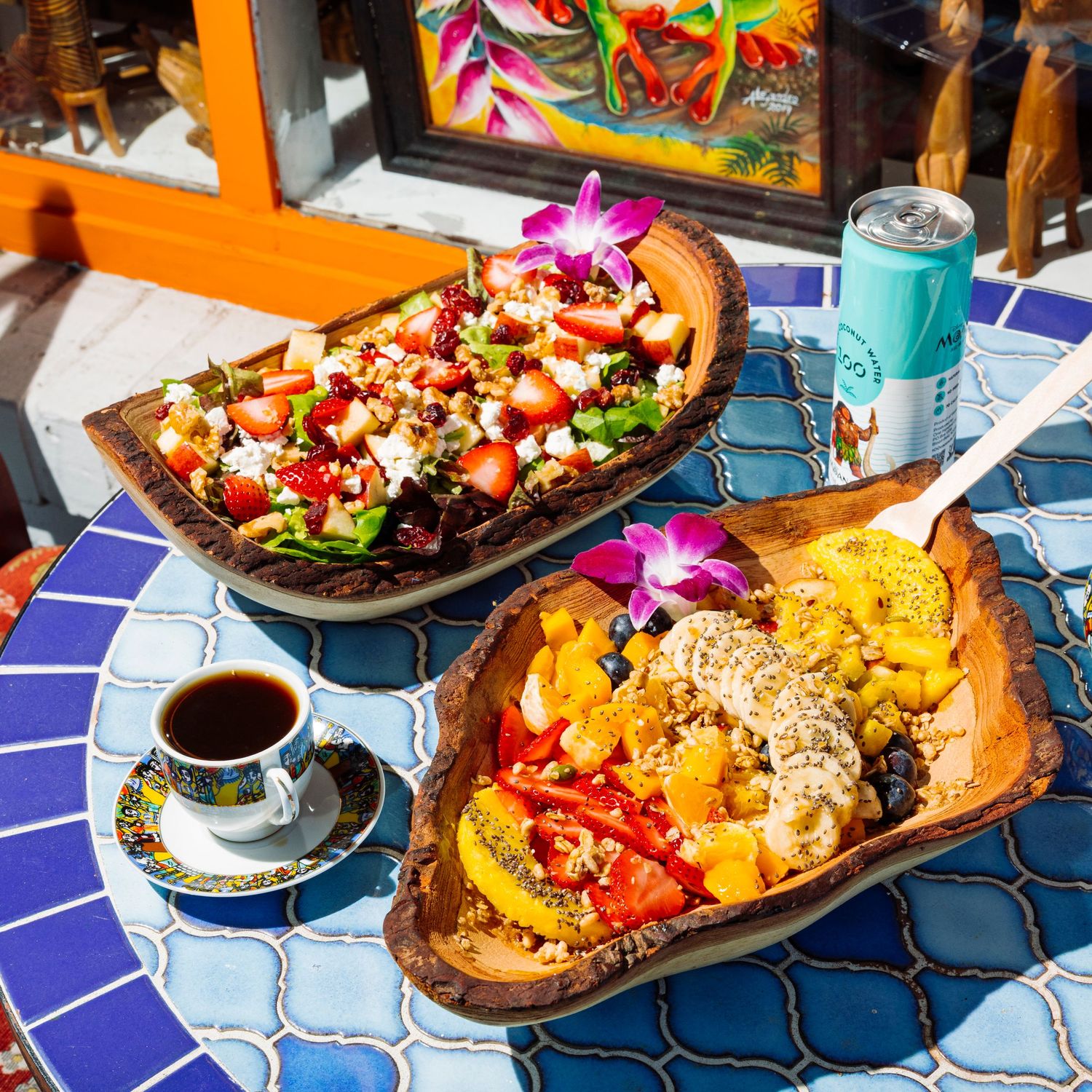 Colorful tropical bowls filled with fresh fruit and salad on a blue mosaic table.