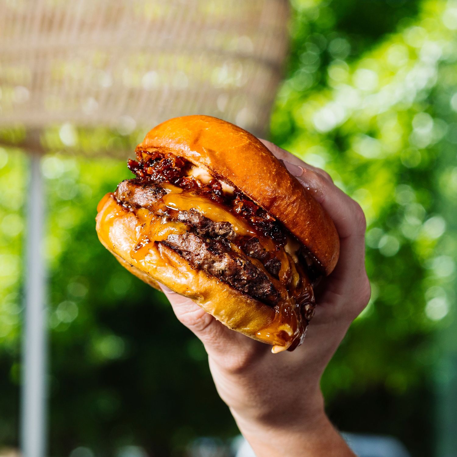 Series of hands holding juicy cheeseburgers with melted cheese dripping down the sides.