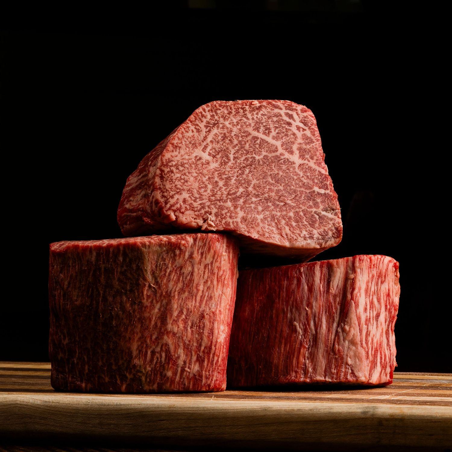 Side view of thick premium raw beef steaks on wooden surface with dramatic lighting.