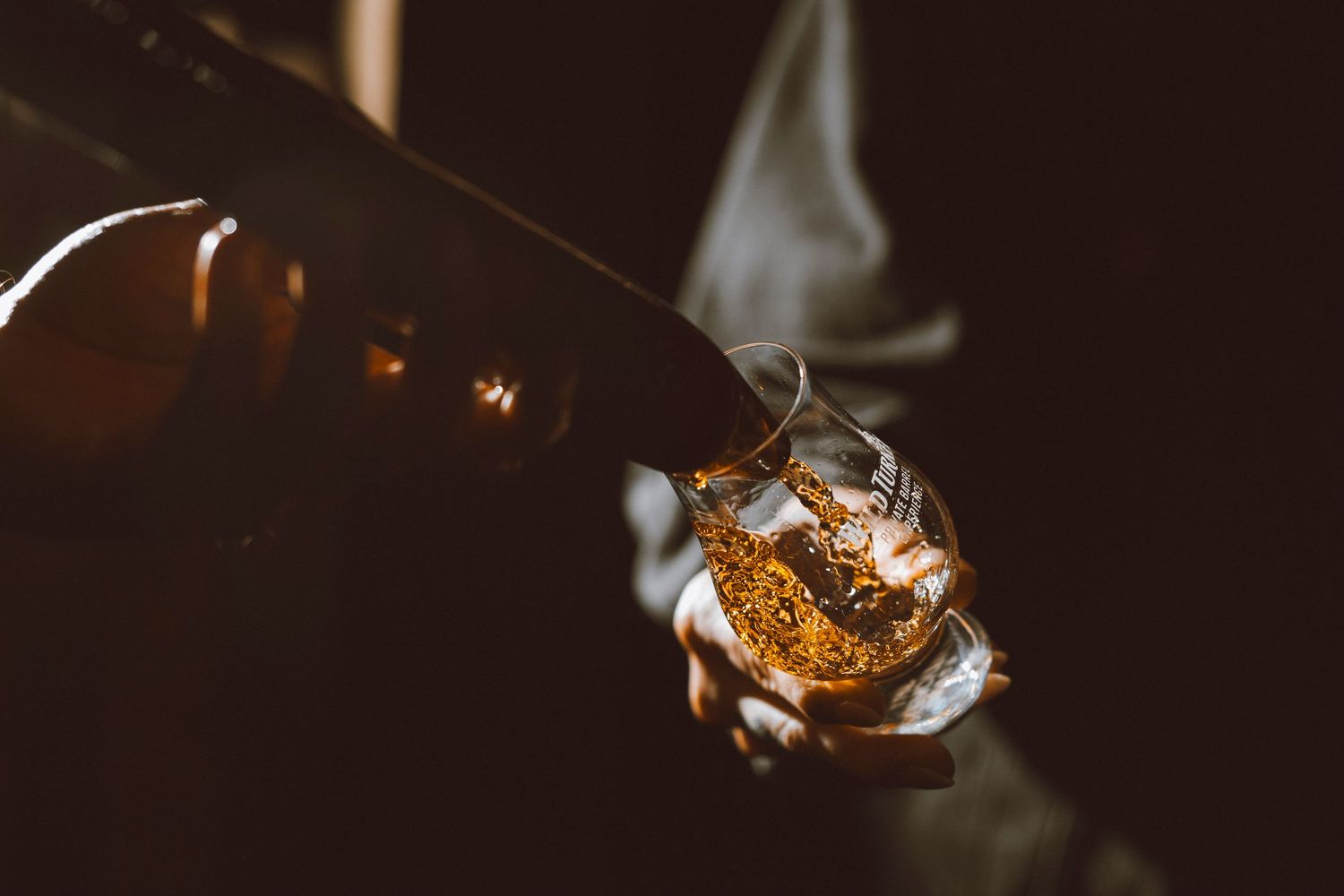 Golden whiskey being poured into a glass with dramatic lighting and smoke effects.