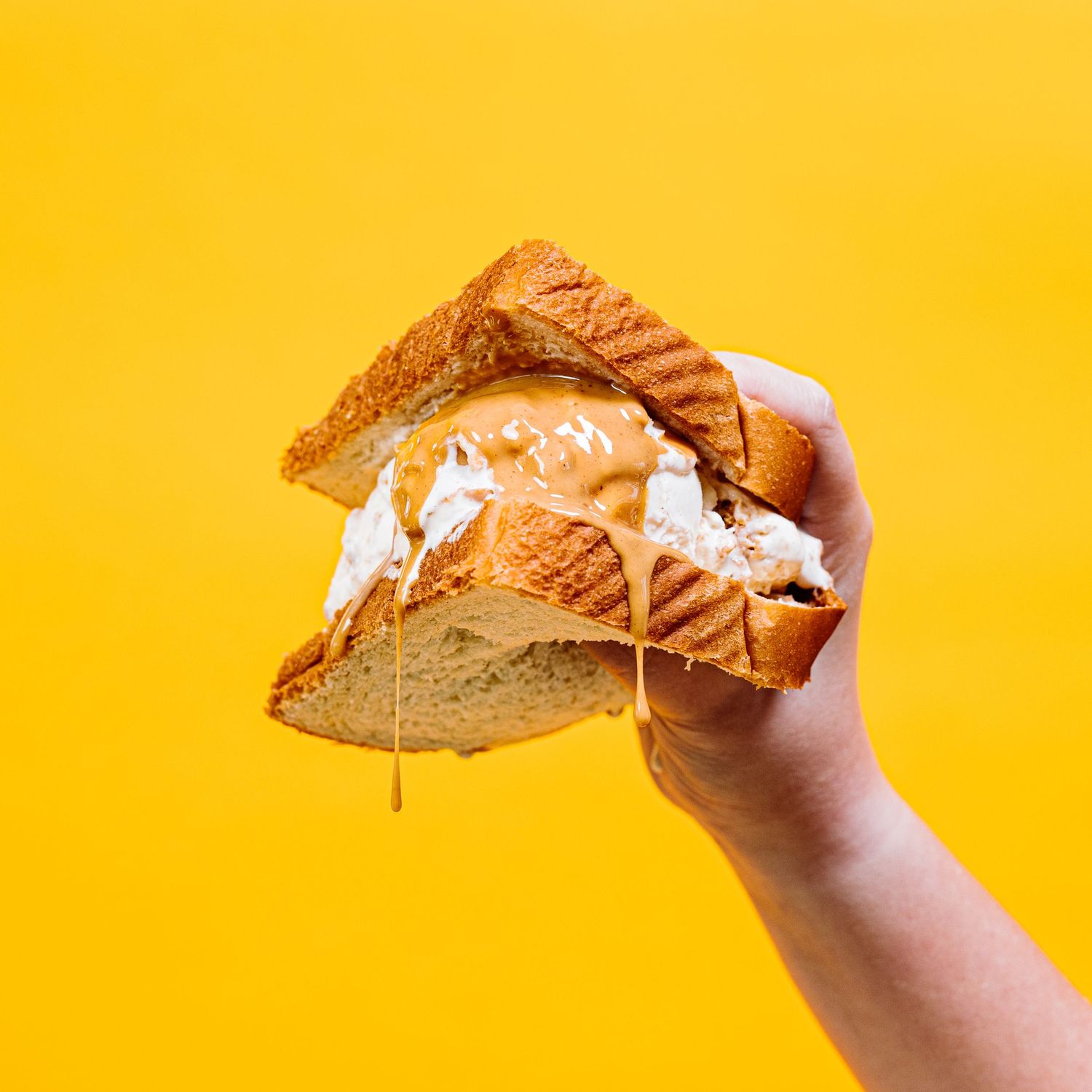 Grilled cheese sandwich with melted cheese dripping down against a bright yellow background.