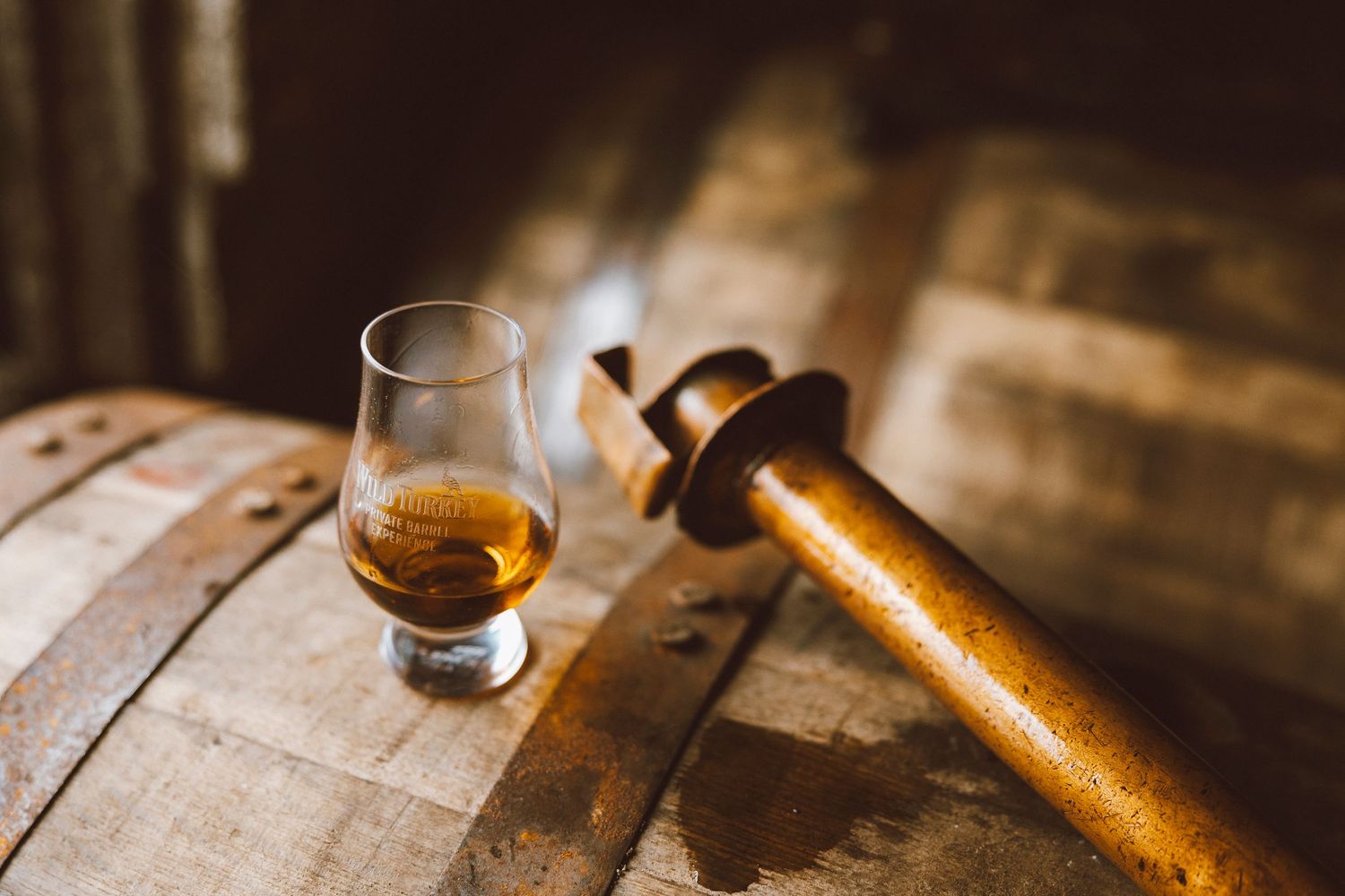 Glencairn whiskey glass and wooden tap on aged wooden barrel.