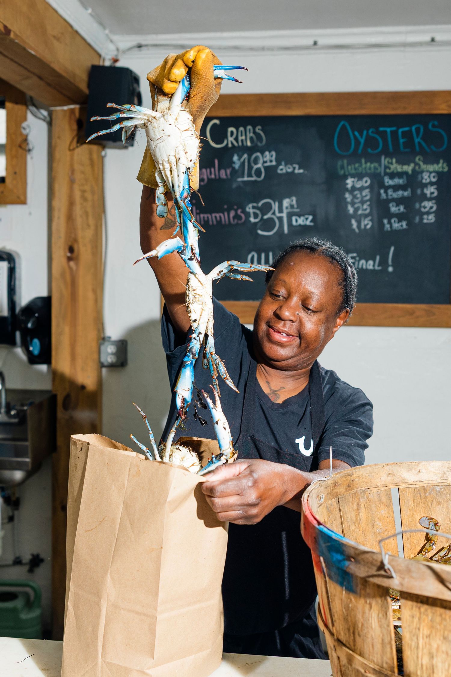 Restaurant worker smiling while preparing takeout orders and placing seafood into brown paper bags at service counter.