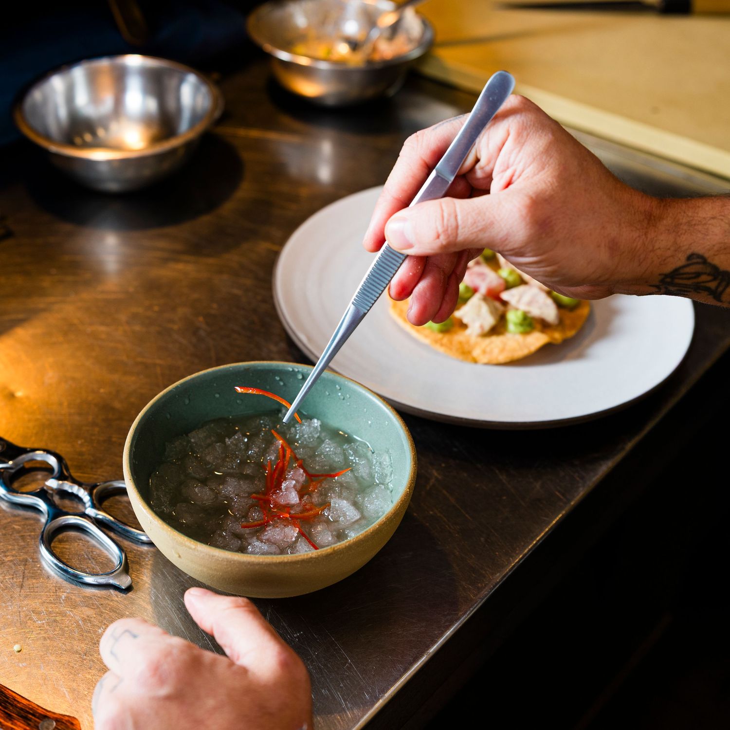 Chef's hands preparing ingredients in metal bowls on dark wooden surface.