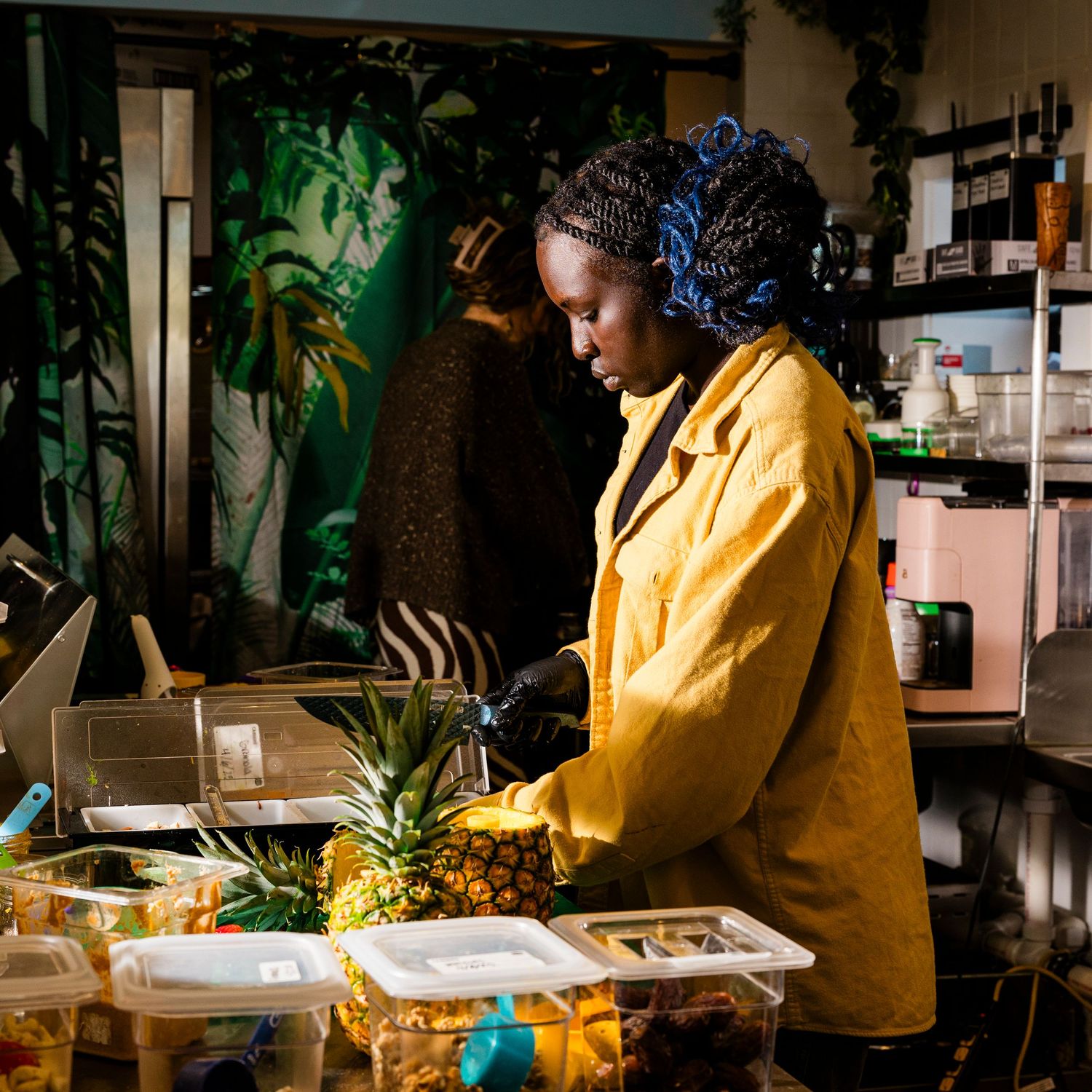 A chef in a yellow coat preparing fresh pineapples in a commercial kitchen.