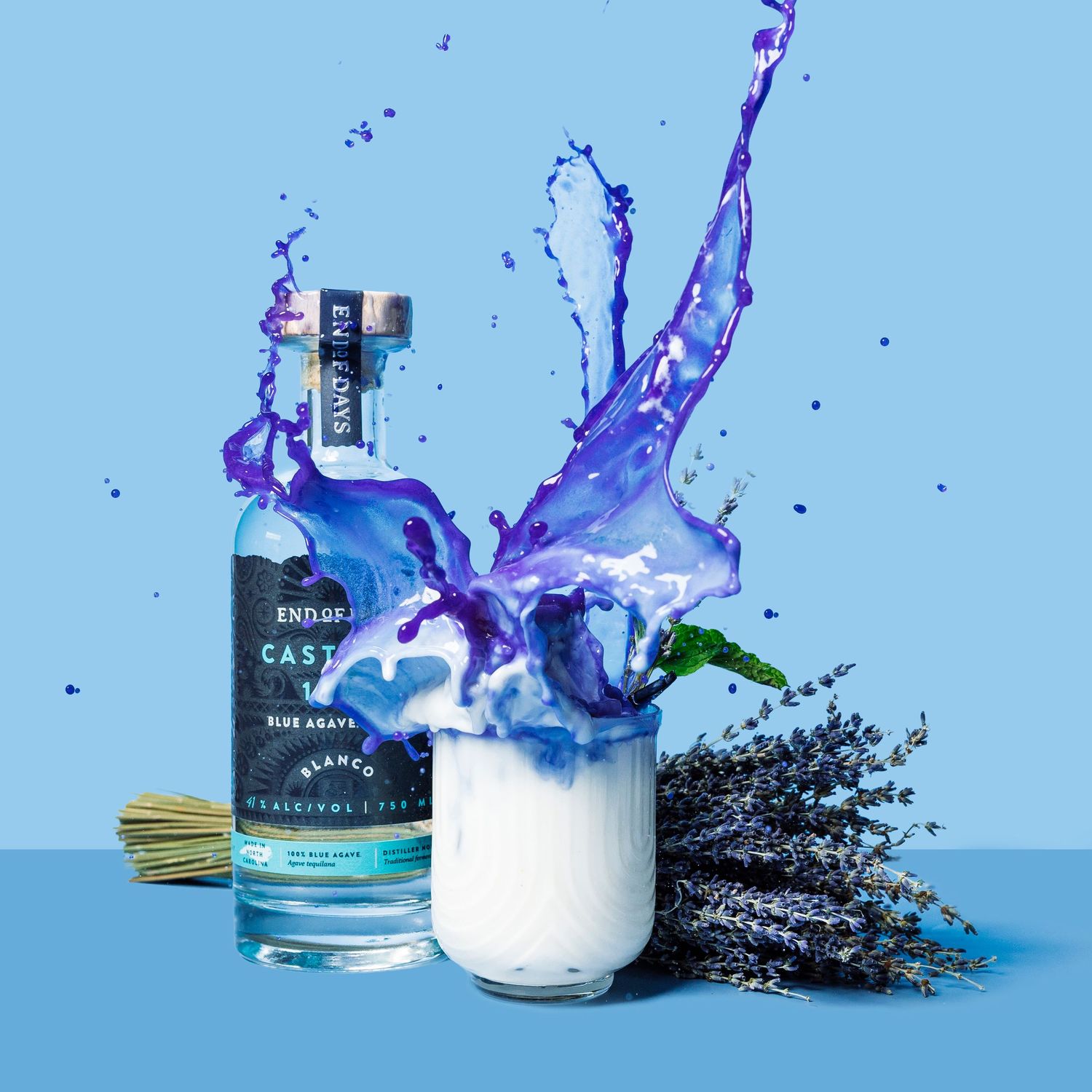 Blue liquids splashing dramatically around bottles and glassware against a light blue background.