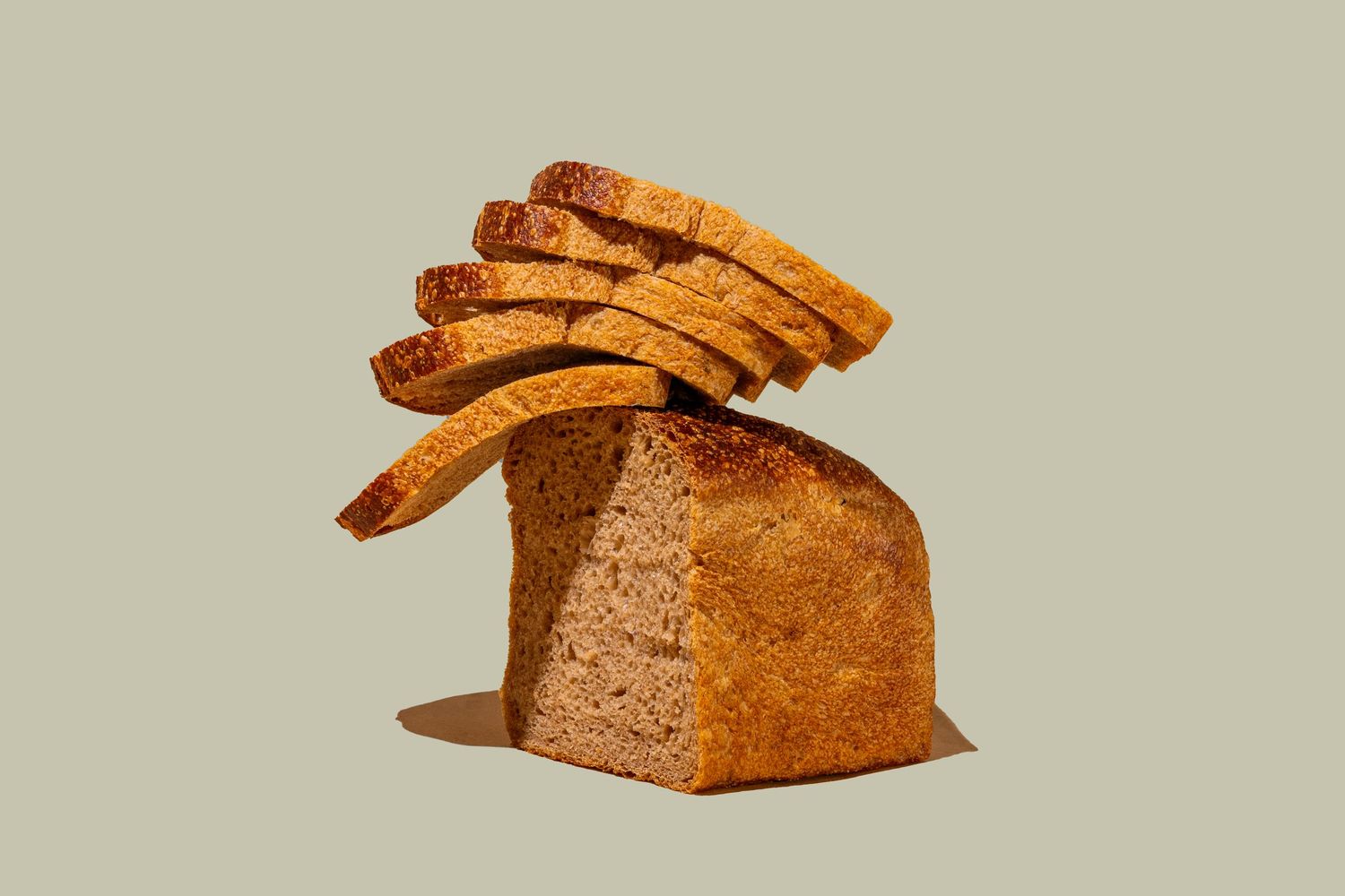 Fresh baked rustic sourdough bread sliced into diagonal pieces on beige surface.