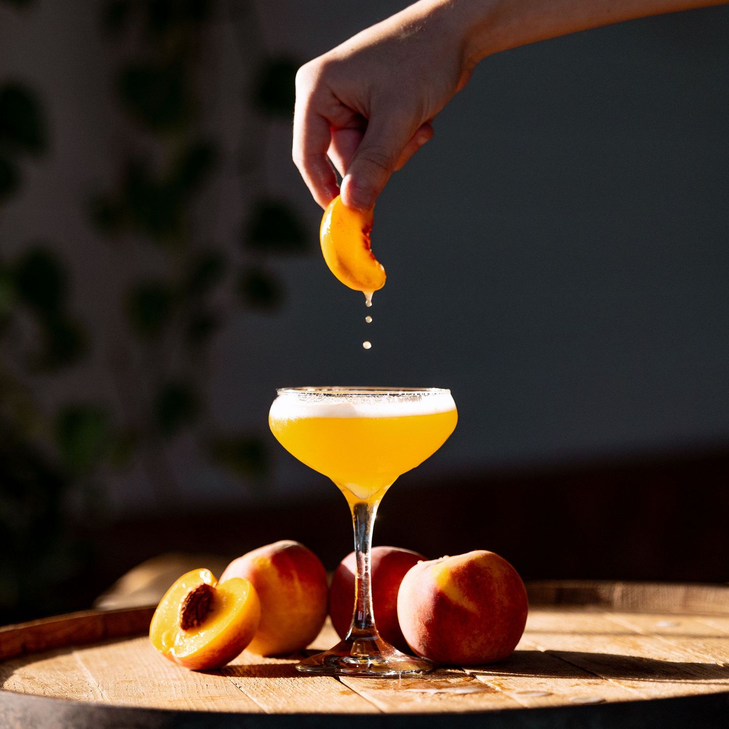 Orange citrus cocktail being prepared with fresh peach garnish in elegant glassware.
