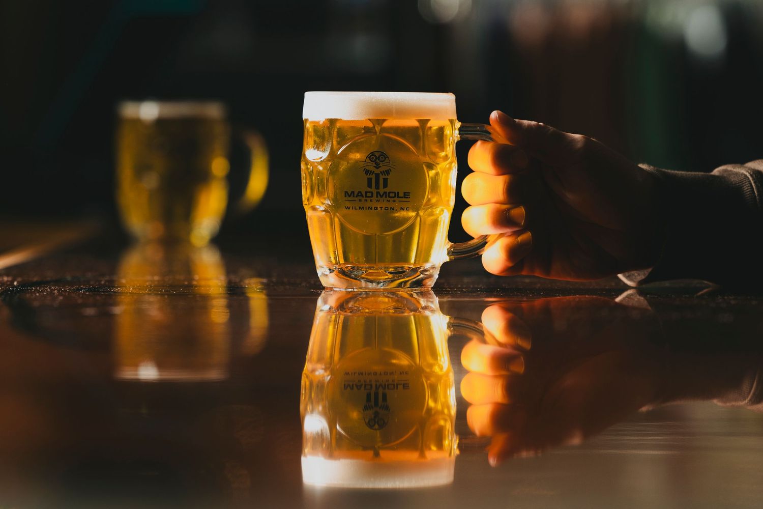 Golden beer in a faceted glass mug reflecting on a dark wooden surface.
