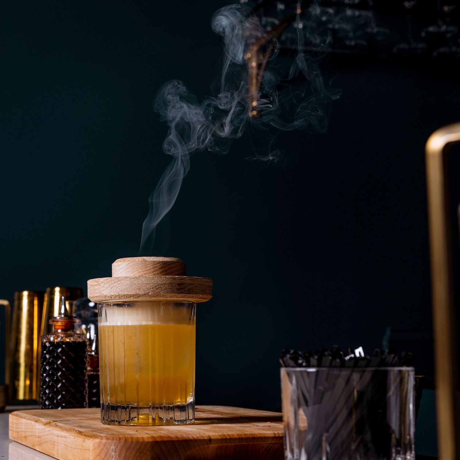 Smoky craft cocktail with wooden lid served on a dark bar counter.