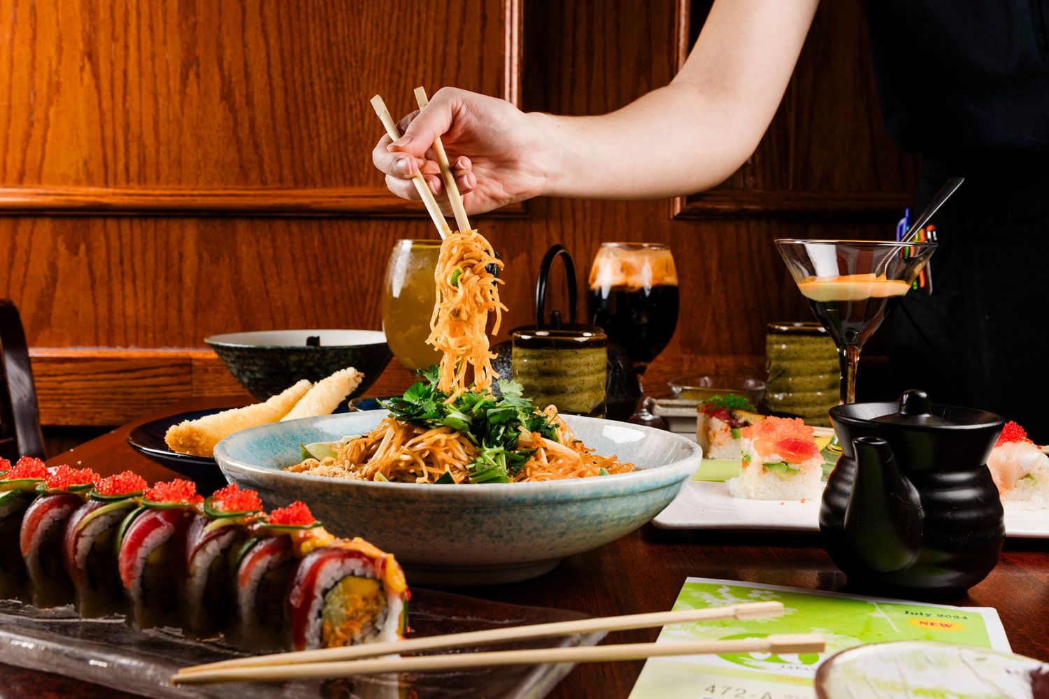 Hands preparing Asian dishes in rustic wooden bowls with fresh ingredients and garnishes.
