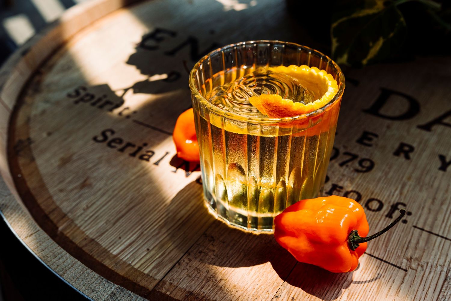 Amber colored cocktails with orange garnishes served in crystal glasses on a rustic wooden surface.