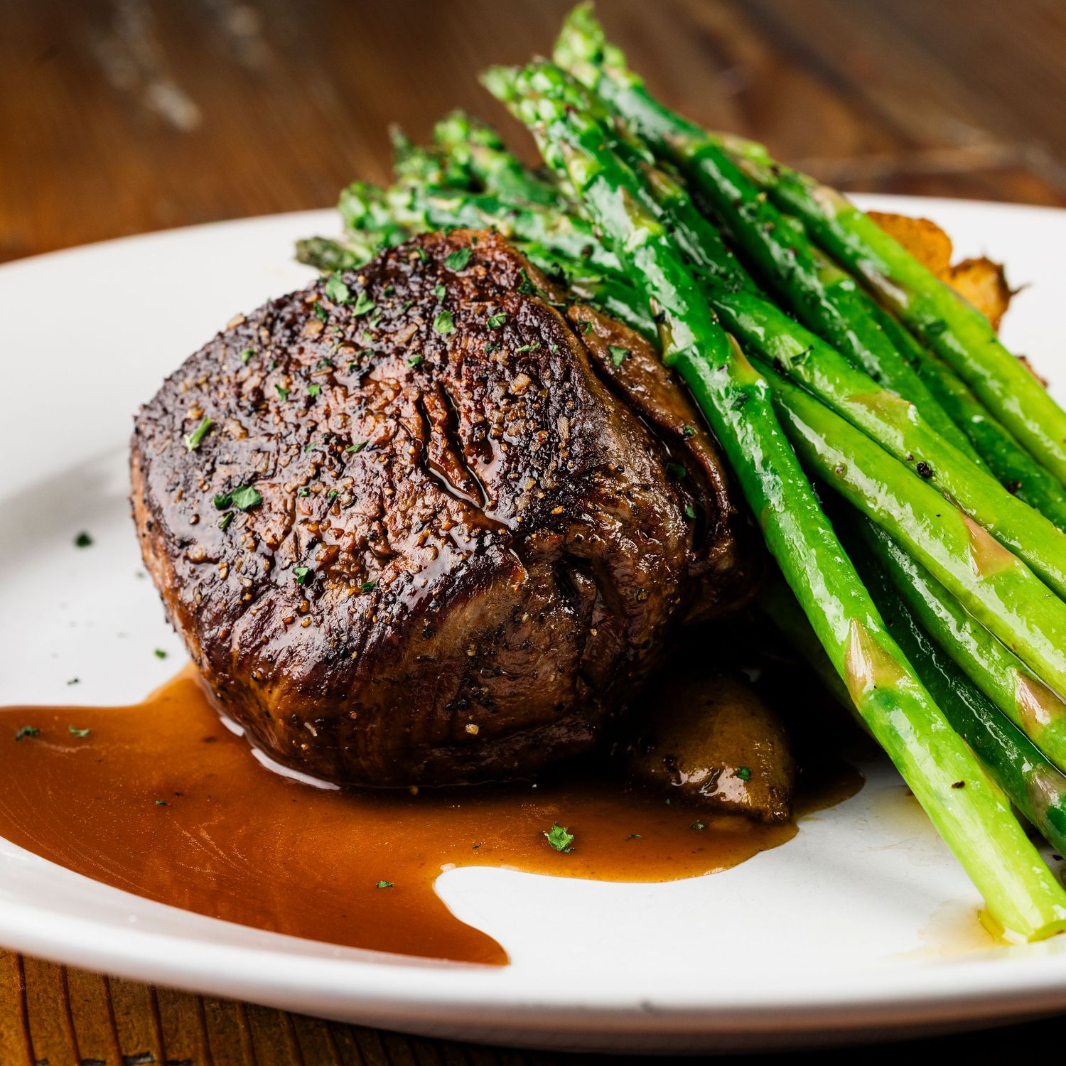 Juicy filet mignon steak with asparagus and brown sauce on a white plate.