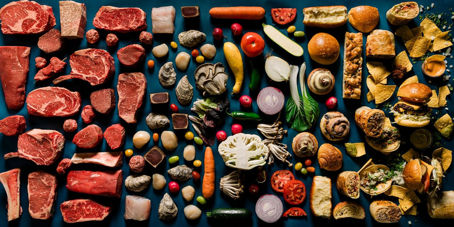 Flat lay composition of raw meats, vegetables, and cooking ingredients arranged in colorful rows.