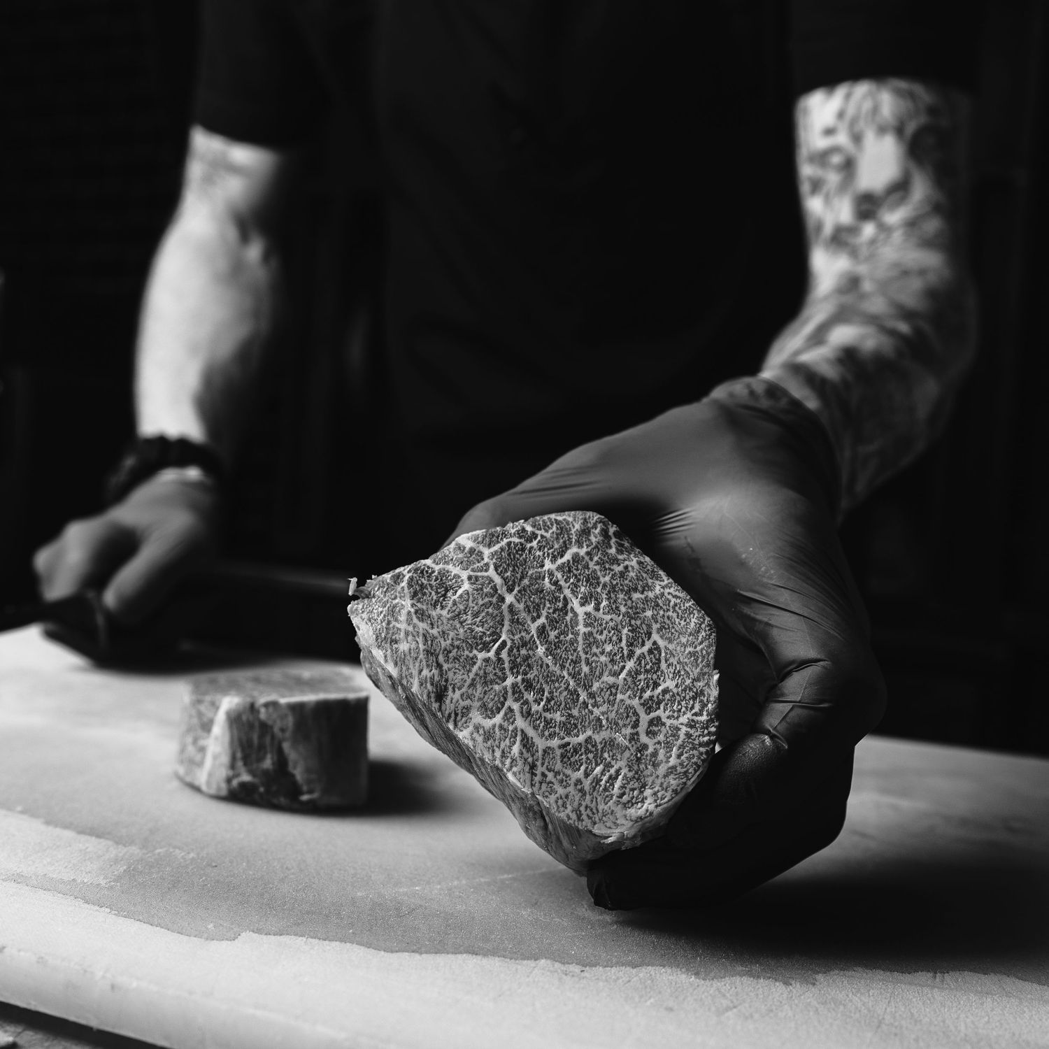 Close-up of gloved hands holding marbled cut of beef against white cutting board.