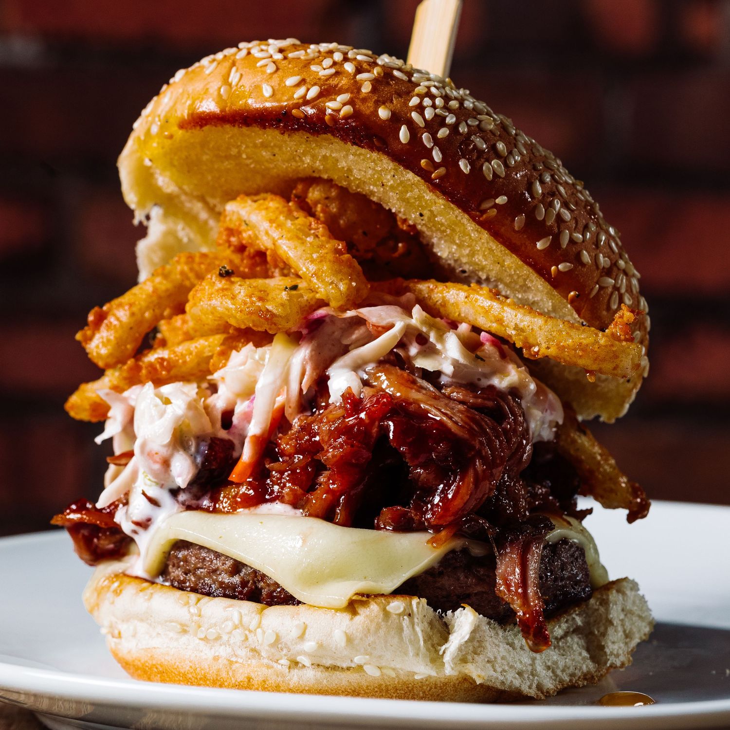 Gourmet burger with melted cheese and bacon dripping sauce on a white plate.