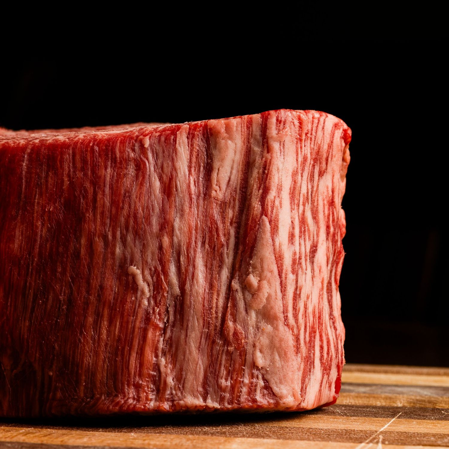Raw beef steaks lined up on wooden cutting board showing different angles and textures.