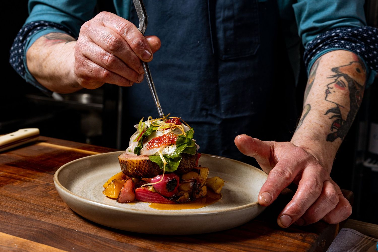 Hands carefully plating and garnishing upscale dishes on white plates.
