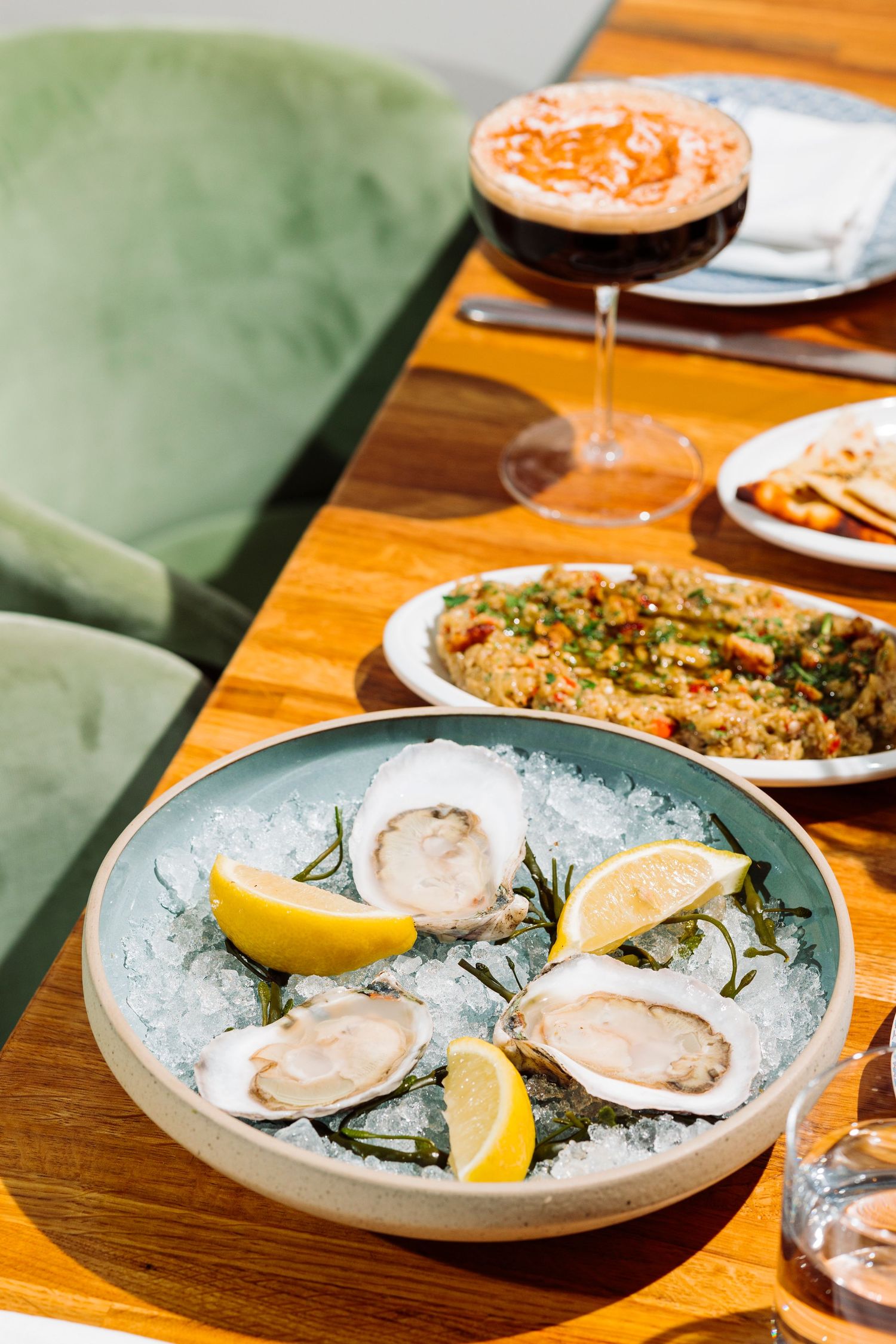 Fresh oysters on ice with lemon wedges served alongside other dishes on wooden table.