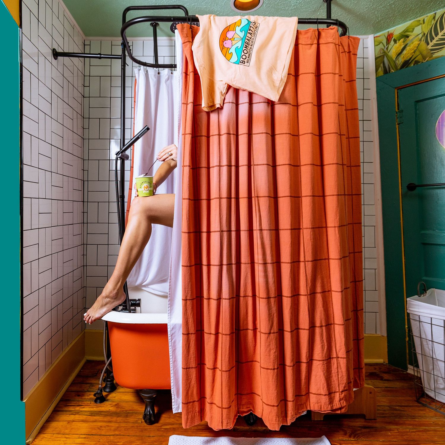 Orange shower curtain in a vintage bathroom with clawfoot tub and white tile walls.