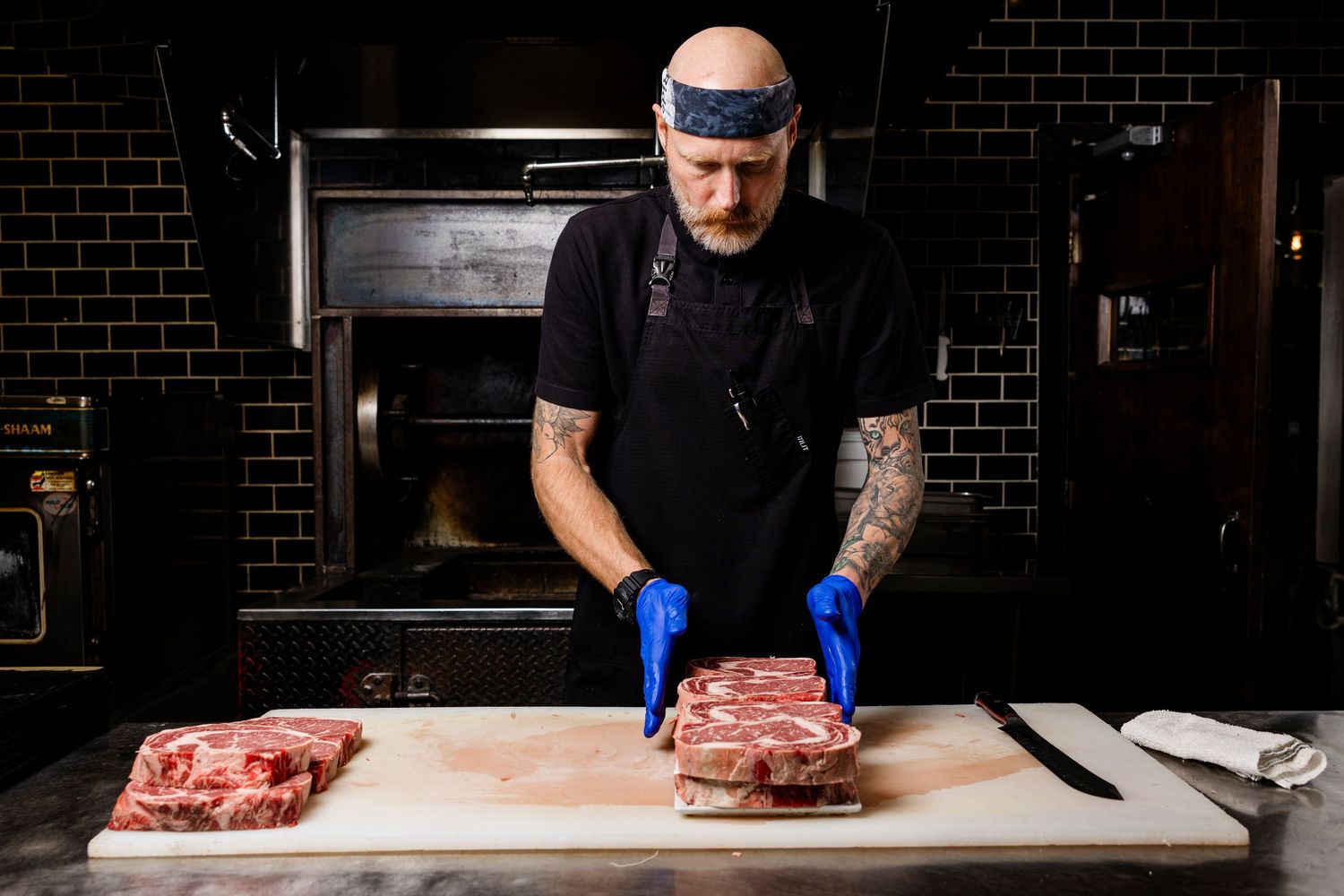 Butcher wearing protective gloves while preparing cuts of meat on wooden board.