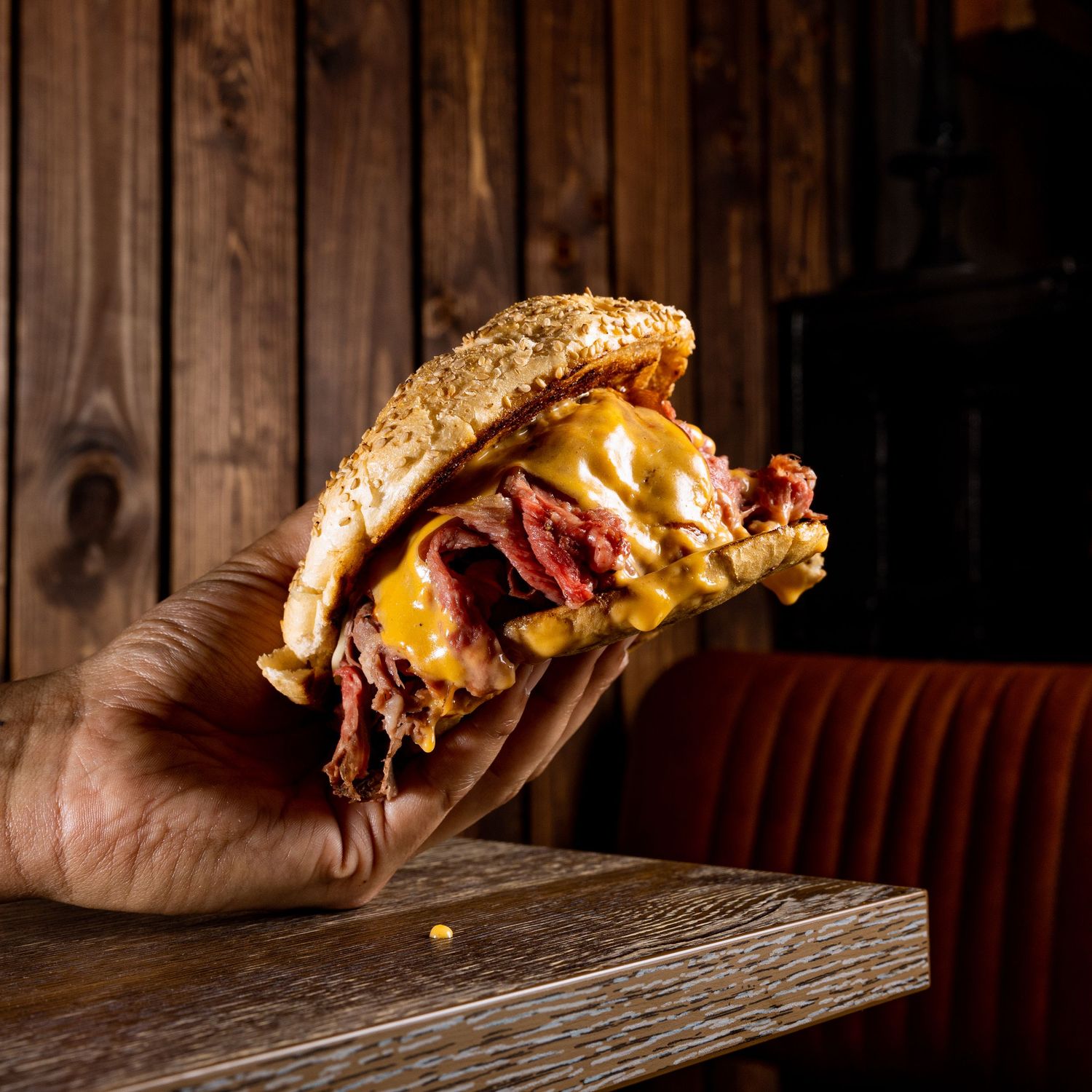 Hands holding melted cheese sandwiches showing dramatic cheese pulls against dark wood background.